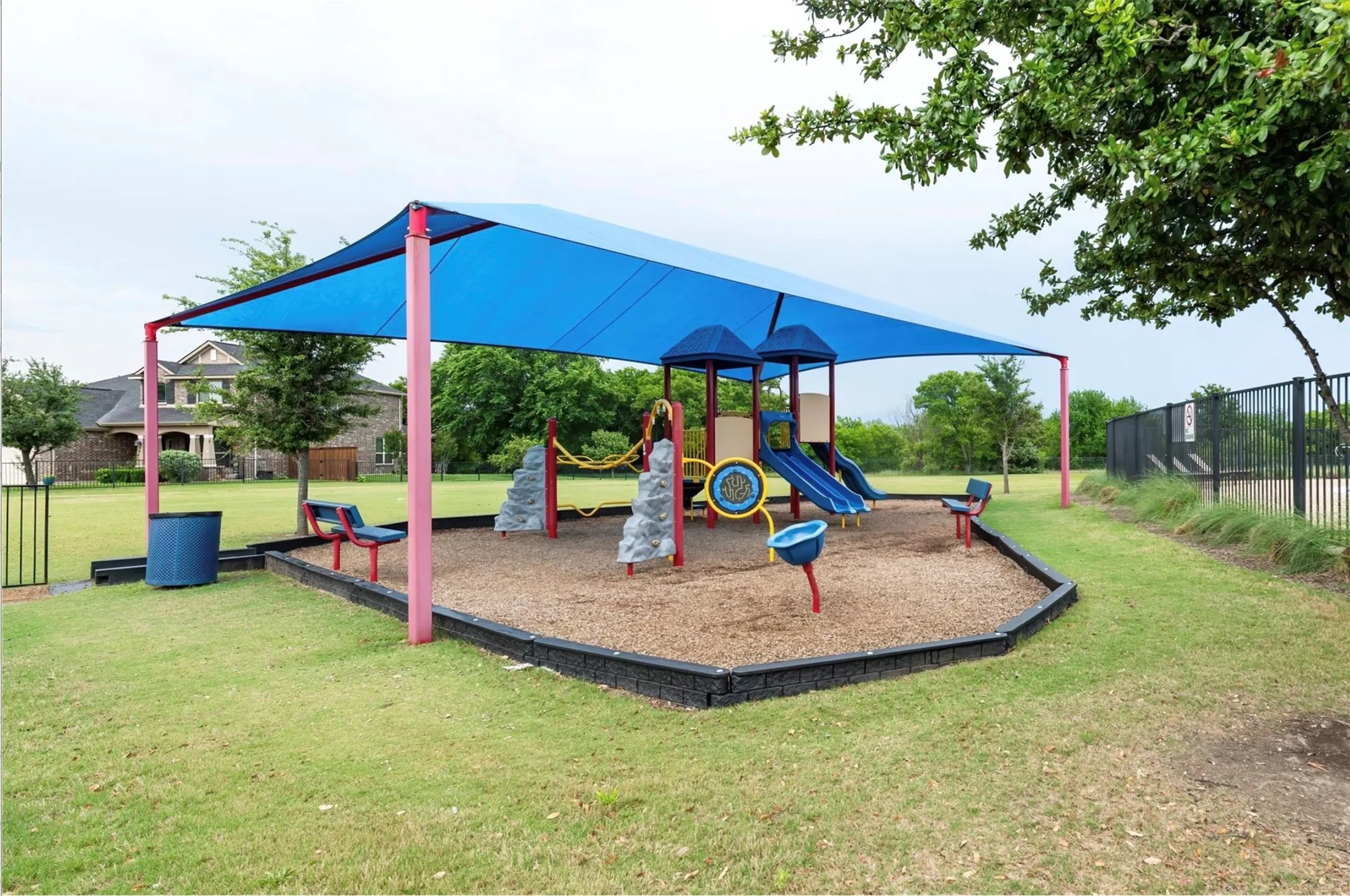 Playground area featuring a blue shade canopy, integrated slides, climbing elements, and rubber mulch surfacing