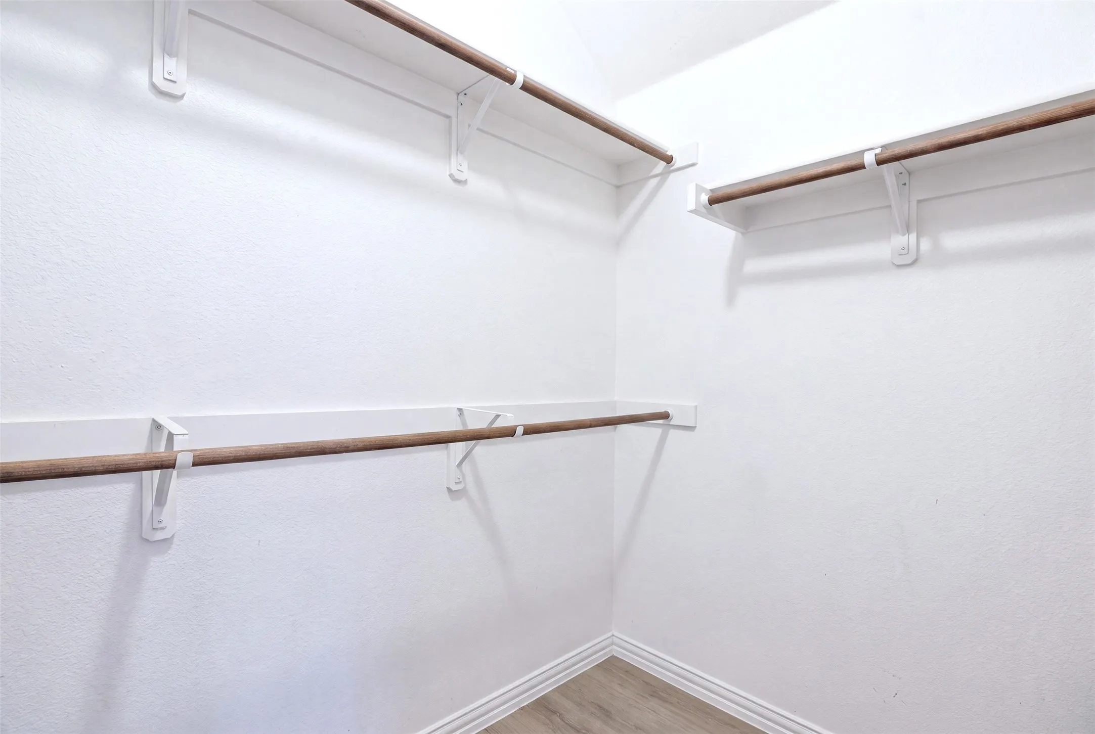 Walk-in closet with multiple hanging rods, white-painted walls, and wood-finish flooring