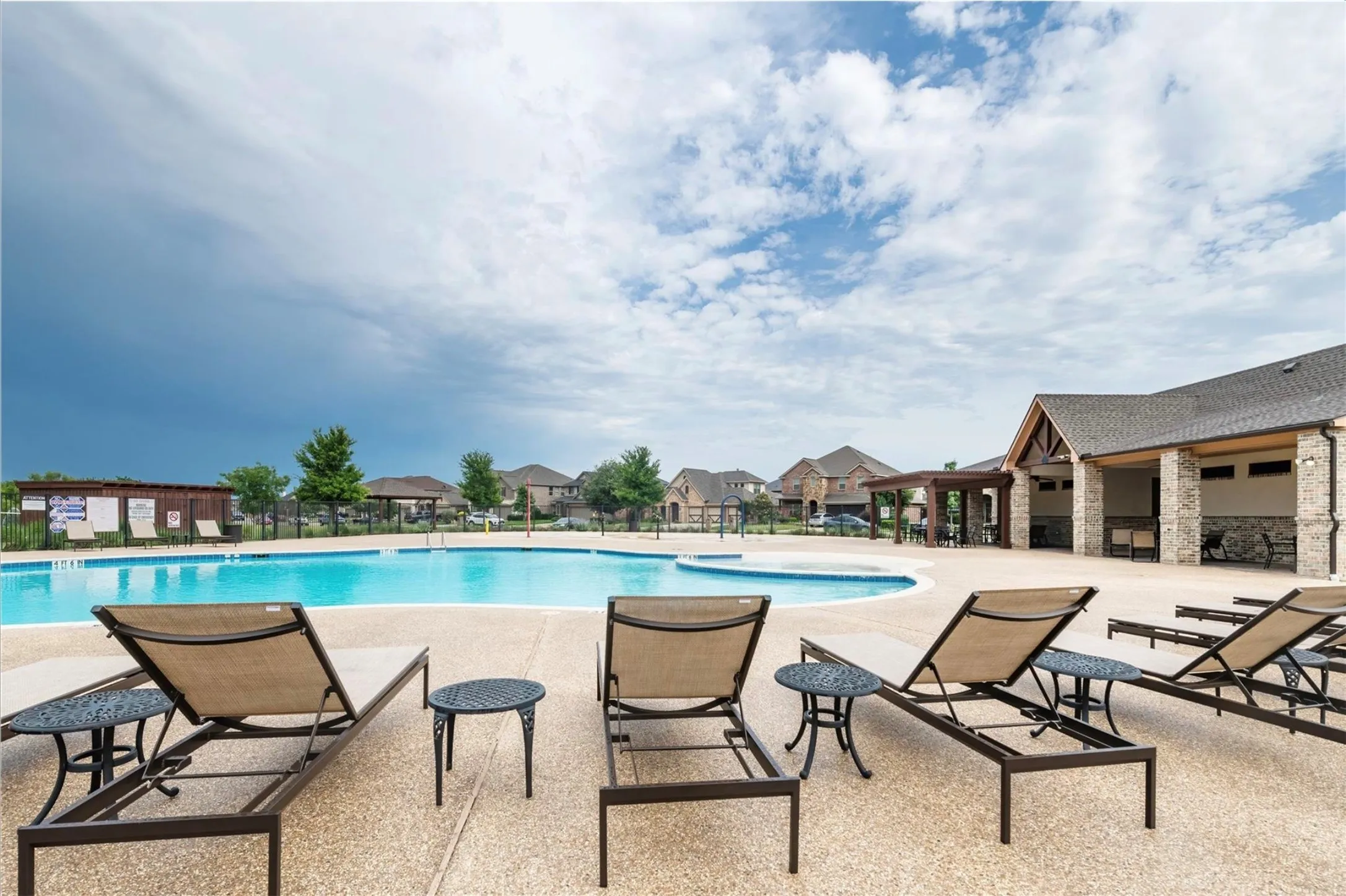 Expansive pool area featuring a curved swimming pool, a clubhouse with stone and timber accents, and a shaded pergola