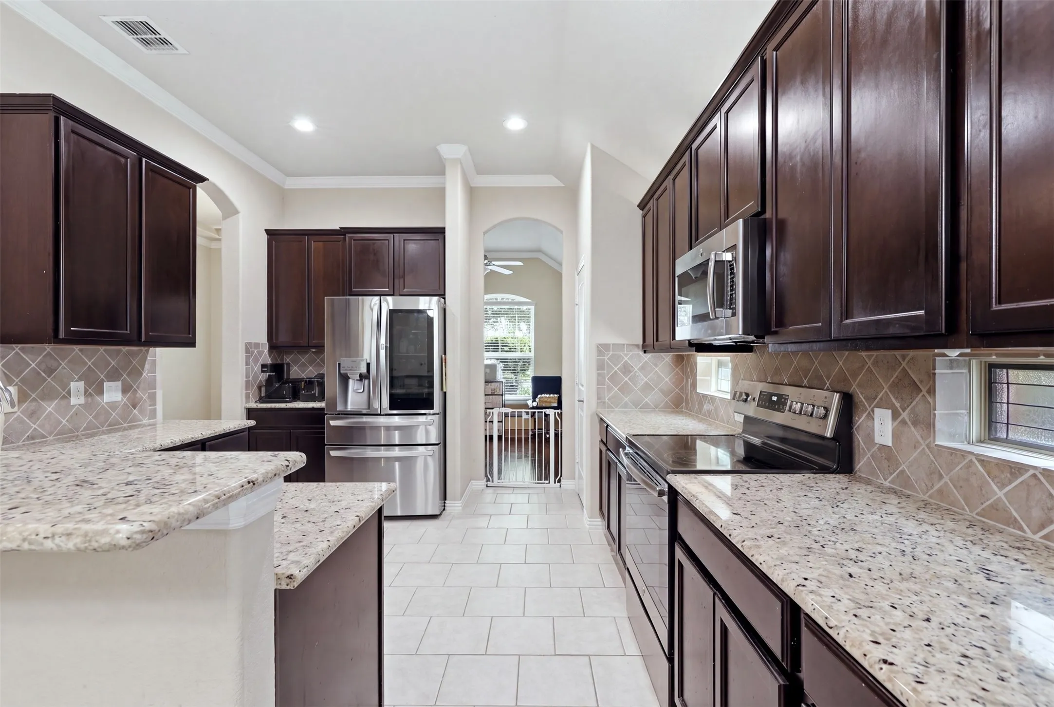 Spacious kitchen featuring extensive dark wood cabinetry, light-toned granite countertops, a tiled backsplash, and stainless steel appliances