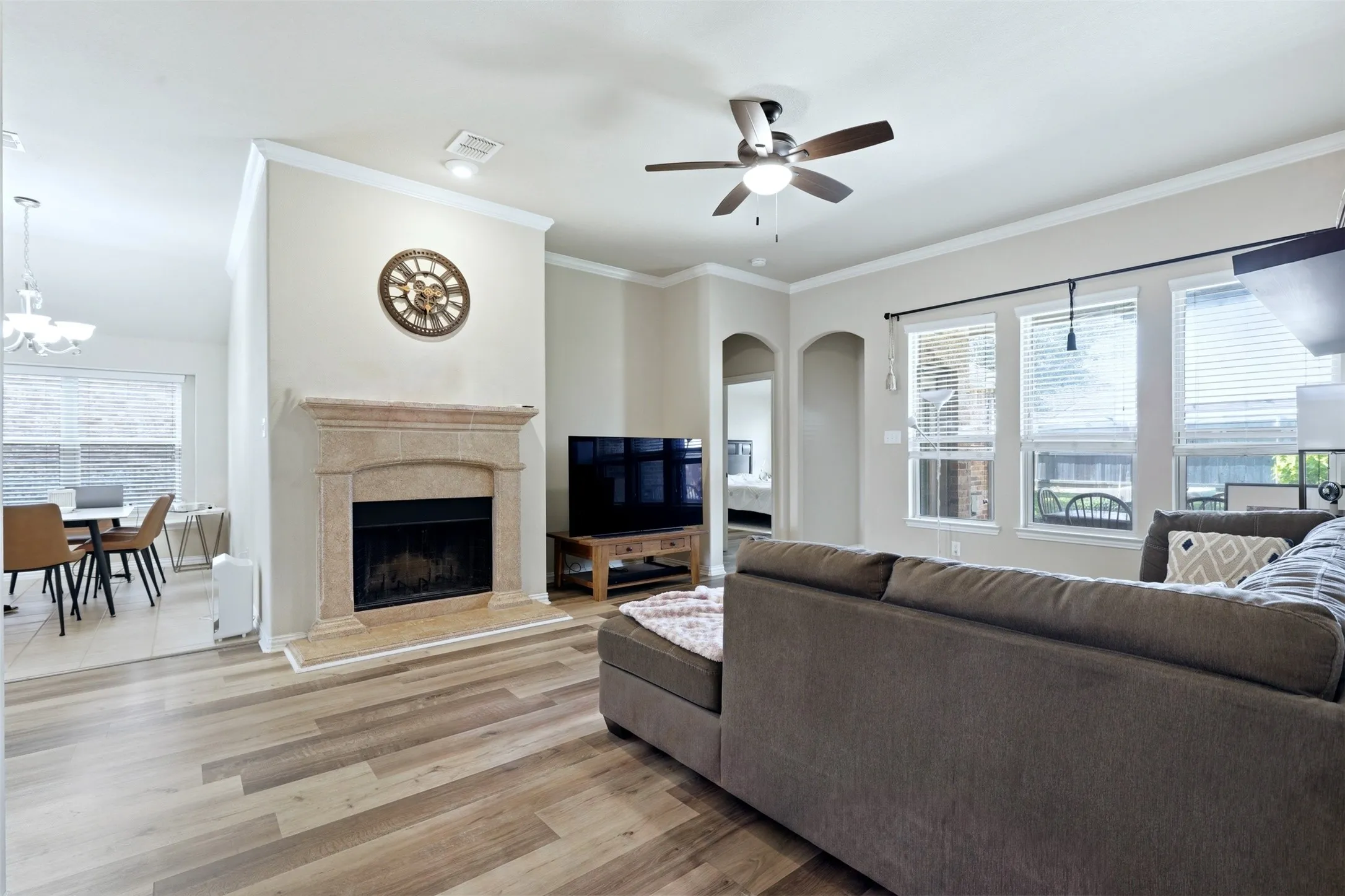 Spacious living area featuring wood-finish flooring, a stone-surround fireplace, and multiple windows