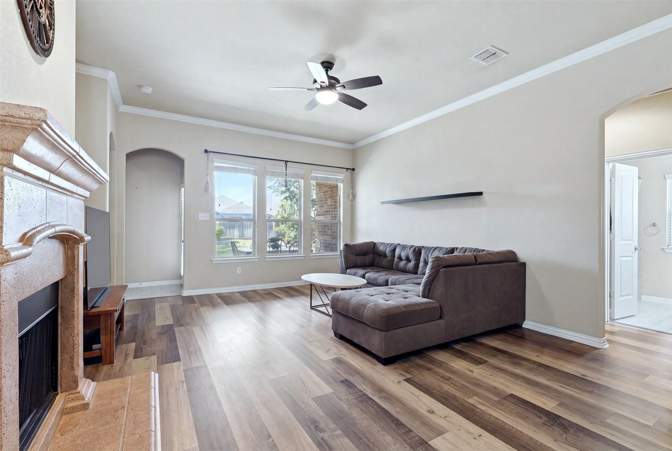 Wood-finish flooring throughout, crown molding, a built-in fireplace with a stone surround, and an arched doorway