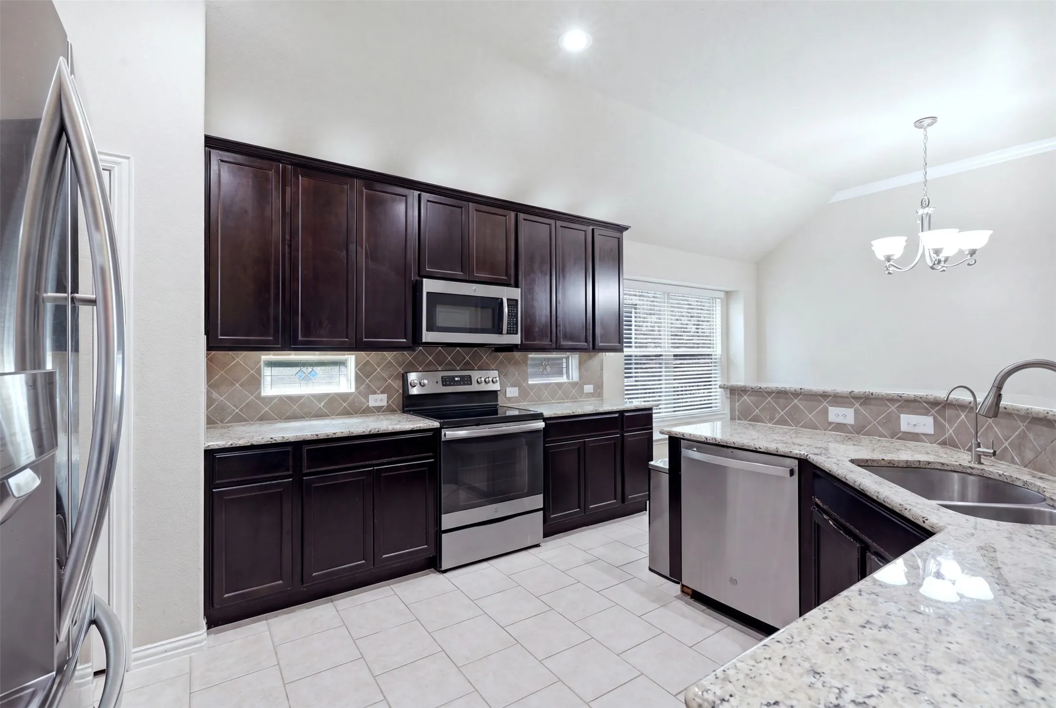 Spacious kitchen featuring dark wood cabinetry, stainless steel appliances, granite countertops, and a tiled backsplash