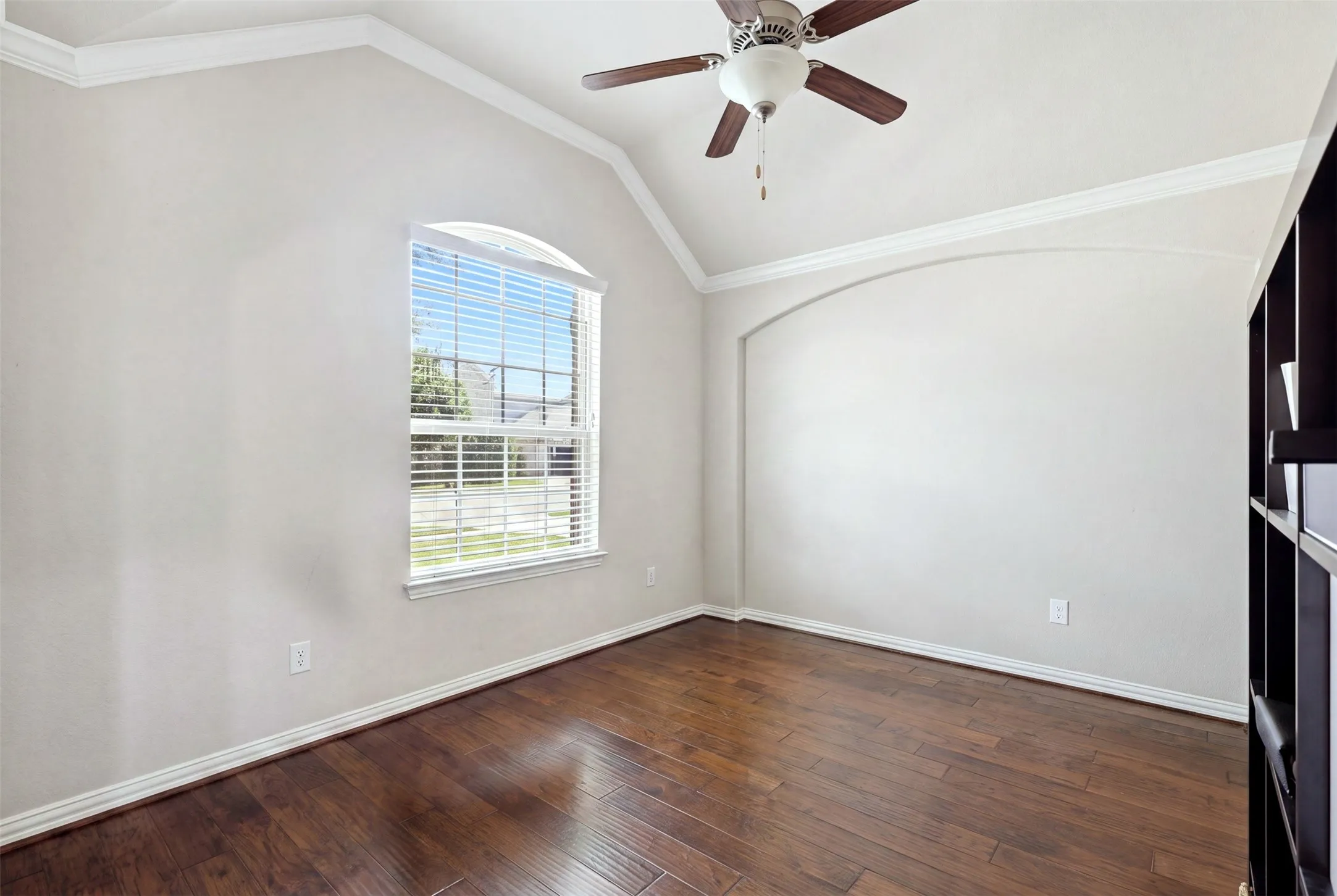 Vaulted ceiling with crown molding, wood-finish flooring, and an arched window with blinds