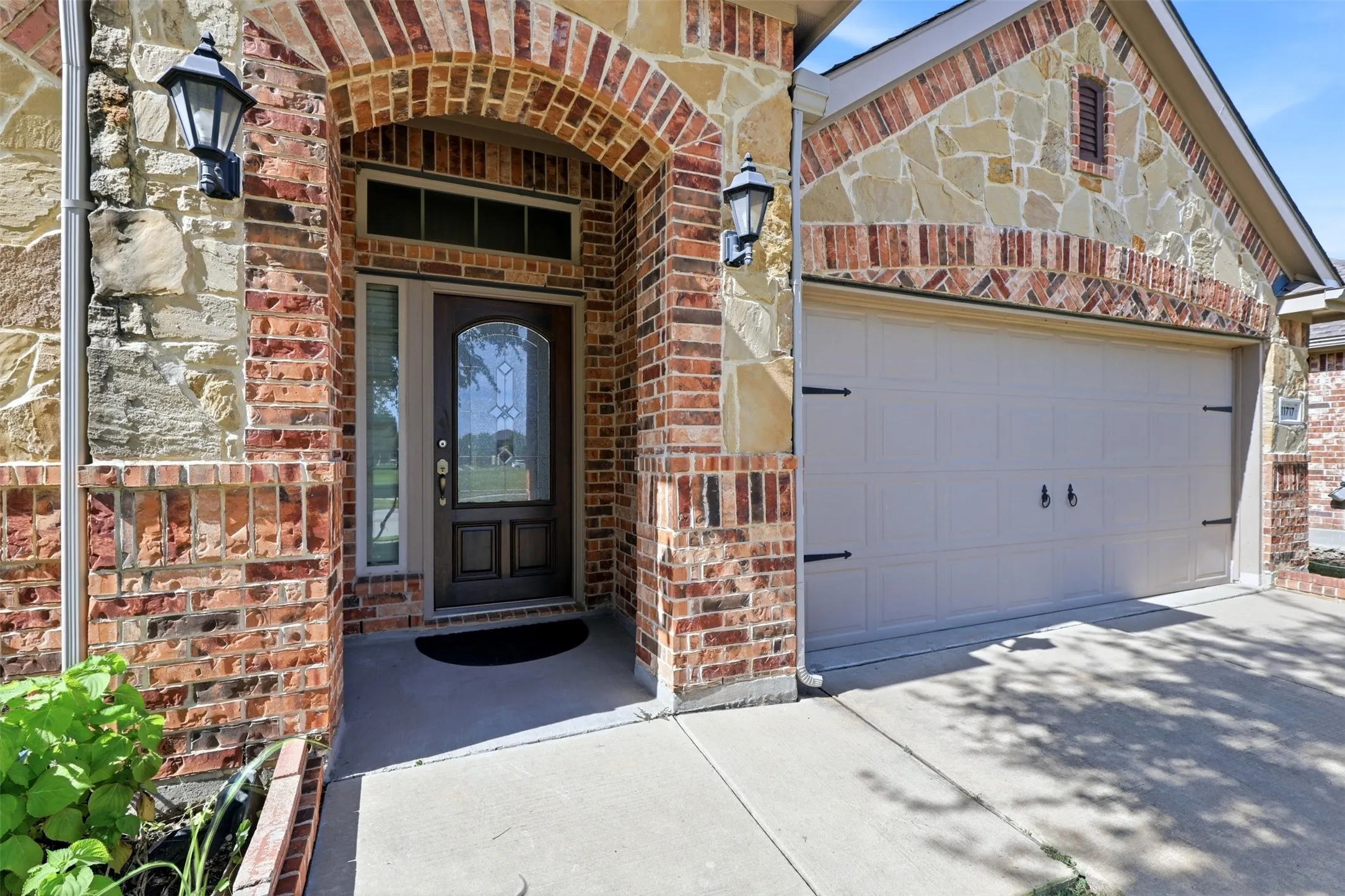 Brick and stone exterior featuring an arched entryway, decorative lighting fixtures, and an integrated garage
