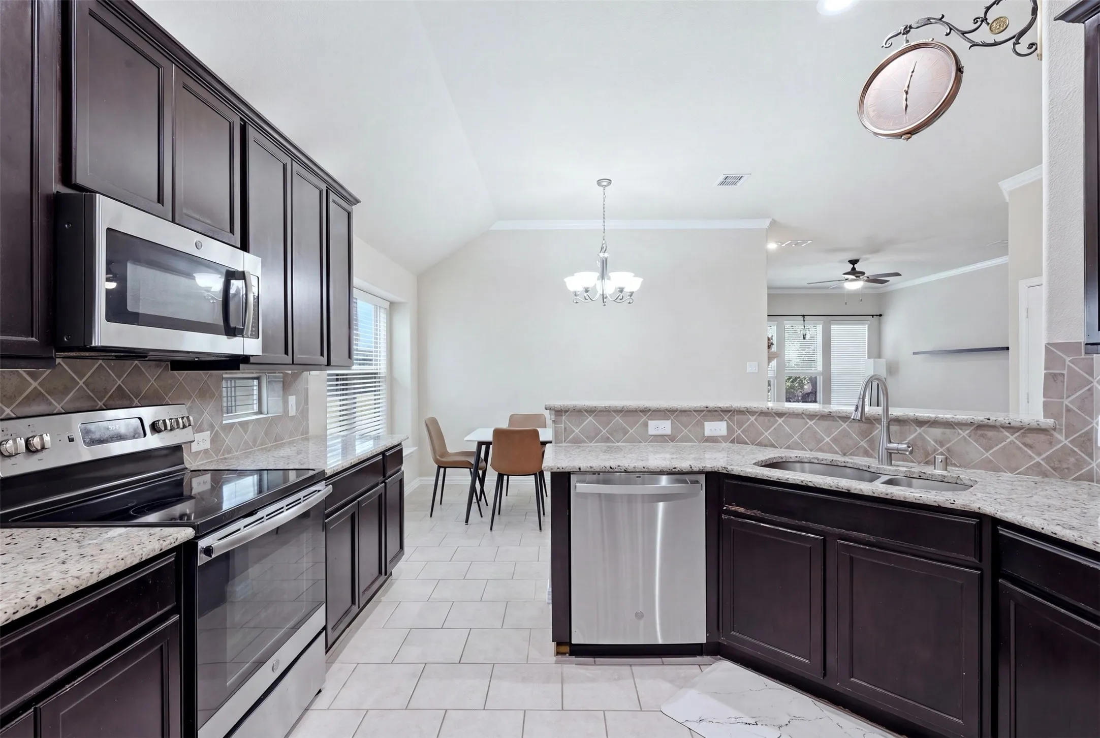 Kitchen featuring dark wood-finish cabinetry, stainless steel appliances, light-toned granite countertops, and a tiled backsplash