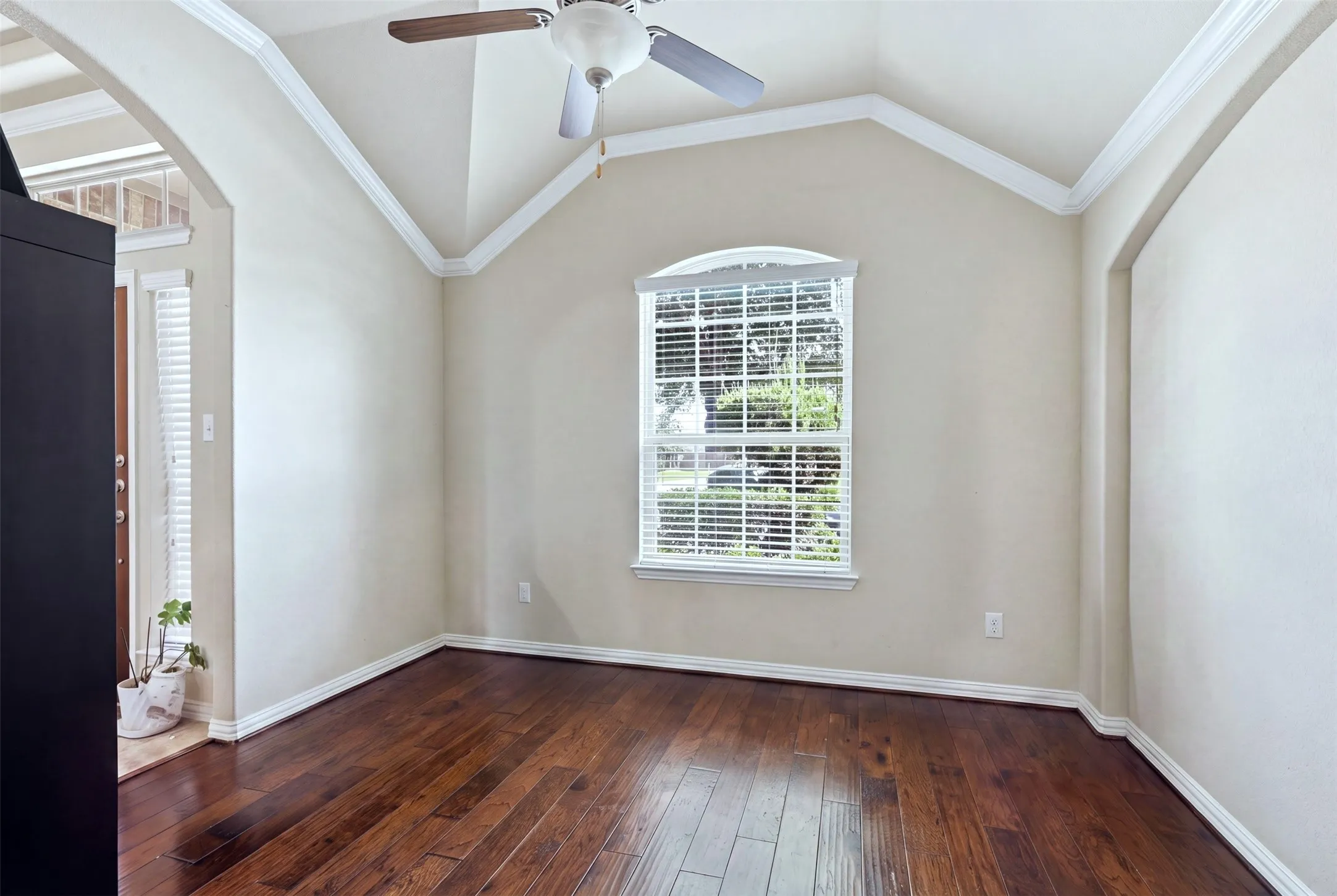 Wood-finish flooring, vaulted ceilings with crown molding, arched entry, and a window with blinds