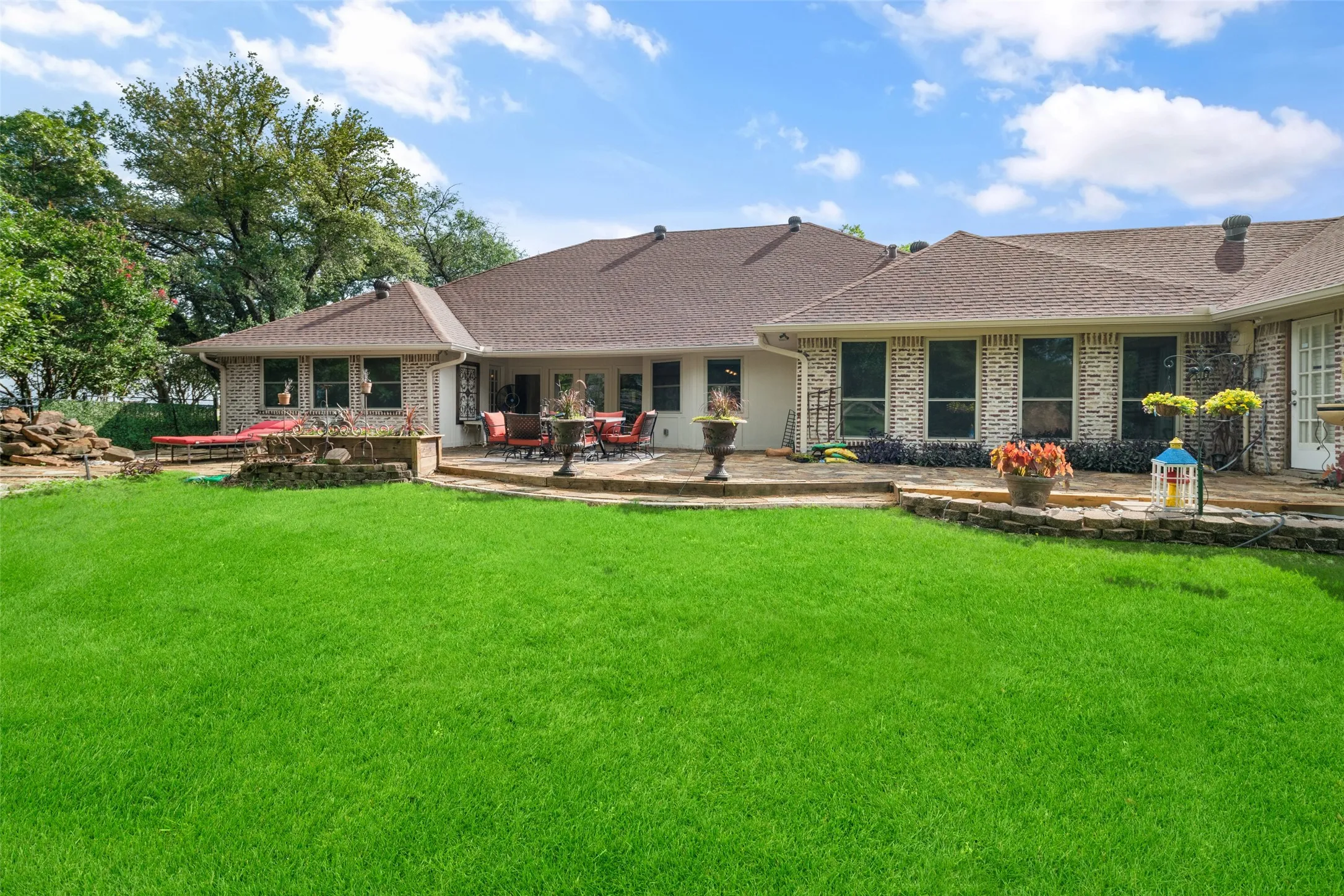 Back of house featuring a yard, a patio area, a shingled roof, and brick siding