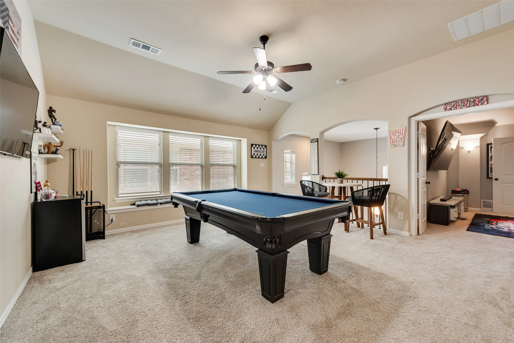 Spacious carpeted room featuring vaulted ceilings, a ceiling fan, and multiple windows with blinds