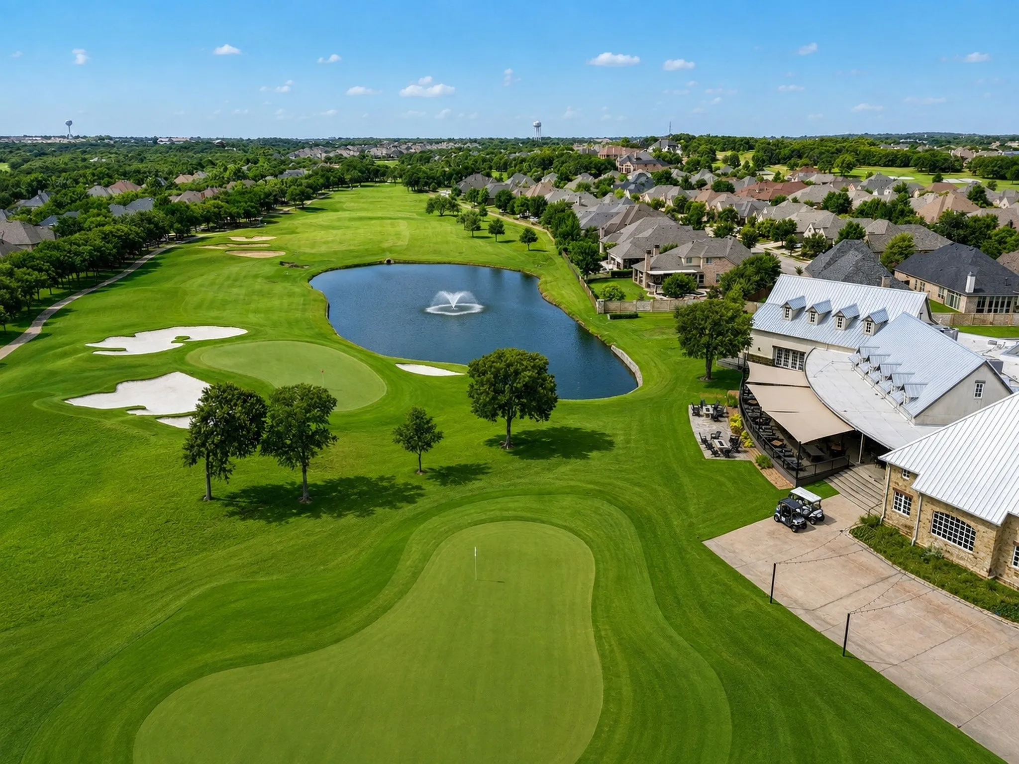 Expansive championship-caliber golf course featuring manicured fairways with strategic bunkering, a pristine water feature with fountain centerpiece, mature specimen trees throughout, and a clubhouse with distinctive architectural detailing visible at the property's edge