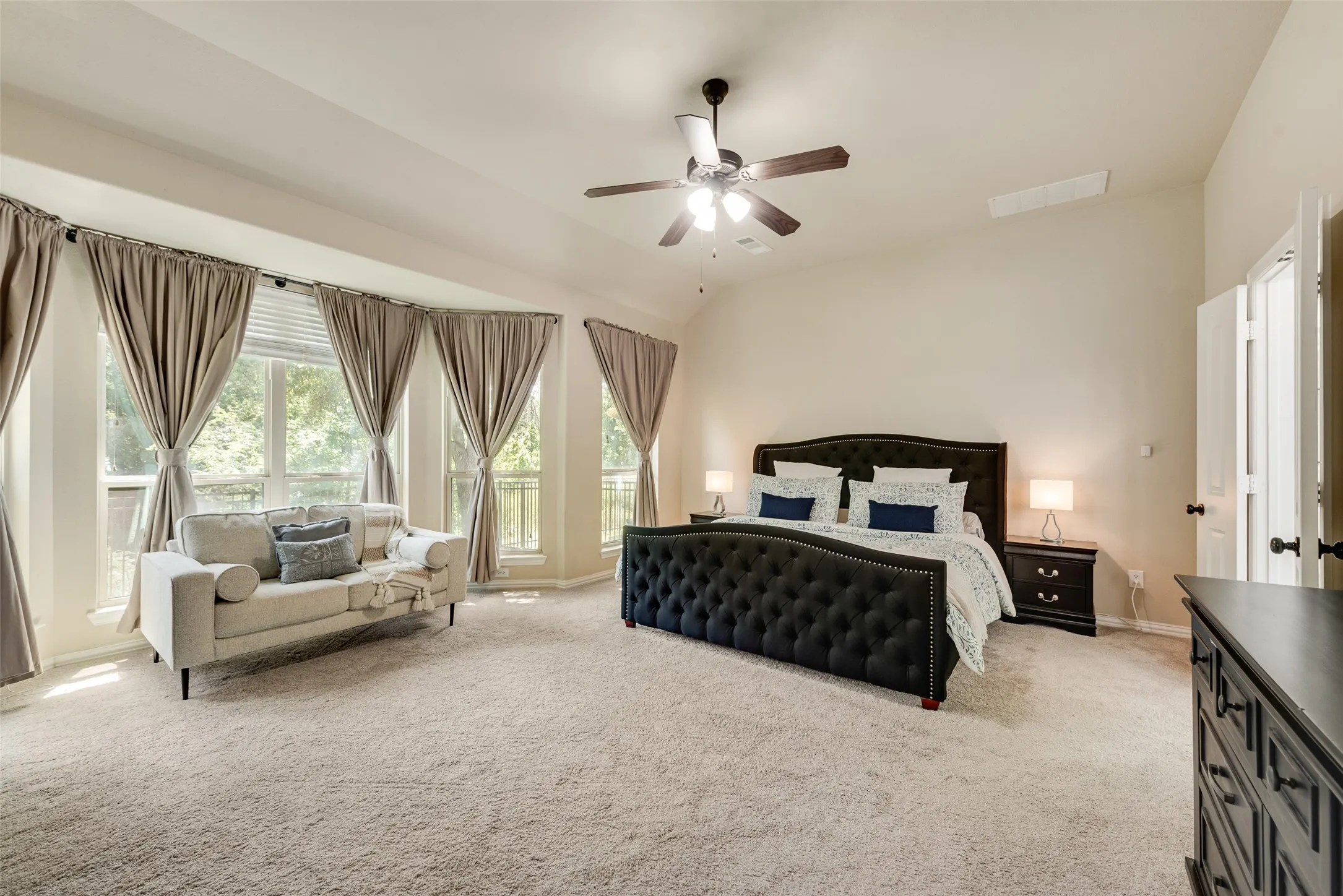 Spacious room featuring vaulted ceilings, a ceiling fan, light-colored carpet flooring, and a bay window configuration with multiple windows