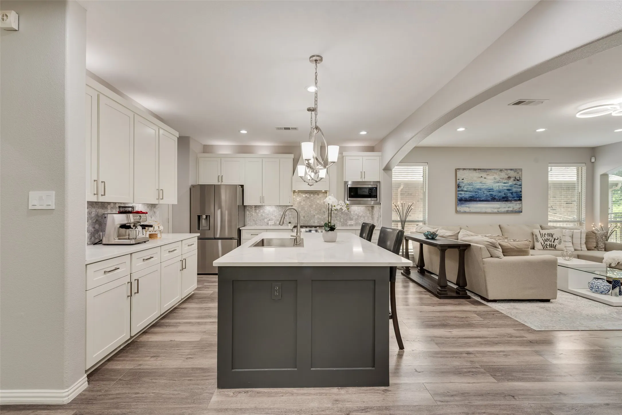 Open-concept kitchen featuring an oversized island with seating, pendant lighting, stainless steel appliances, white cabinetry, and wood-finish flooring
