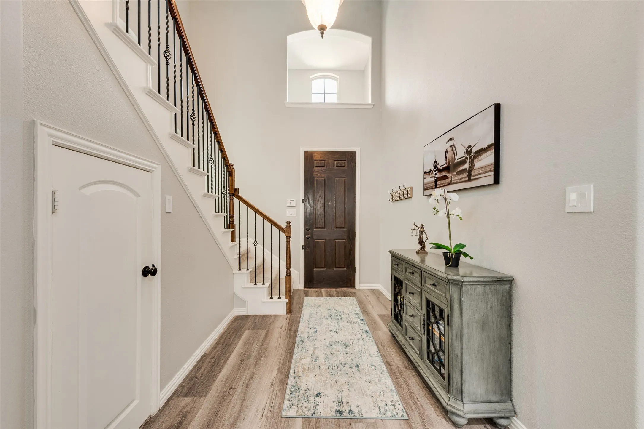Two-story foyer featuring a staircase with wrought iron spindles and wood handrail, wood-finish flooring, a dark wood entry door, and a second-story arched window