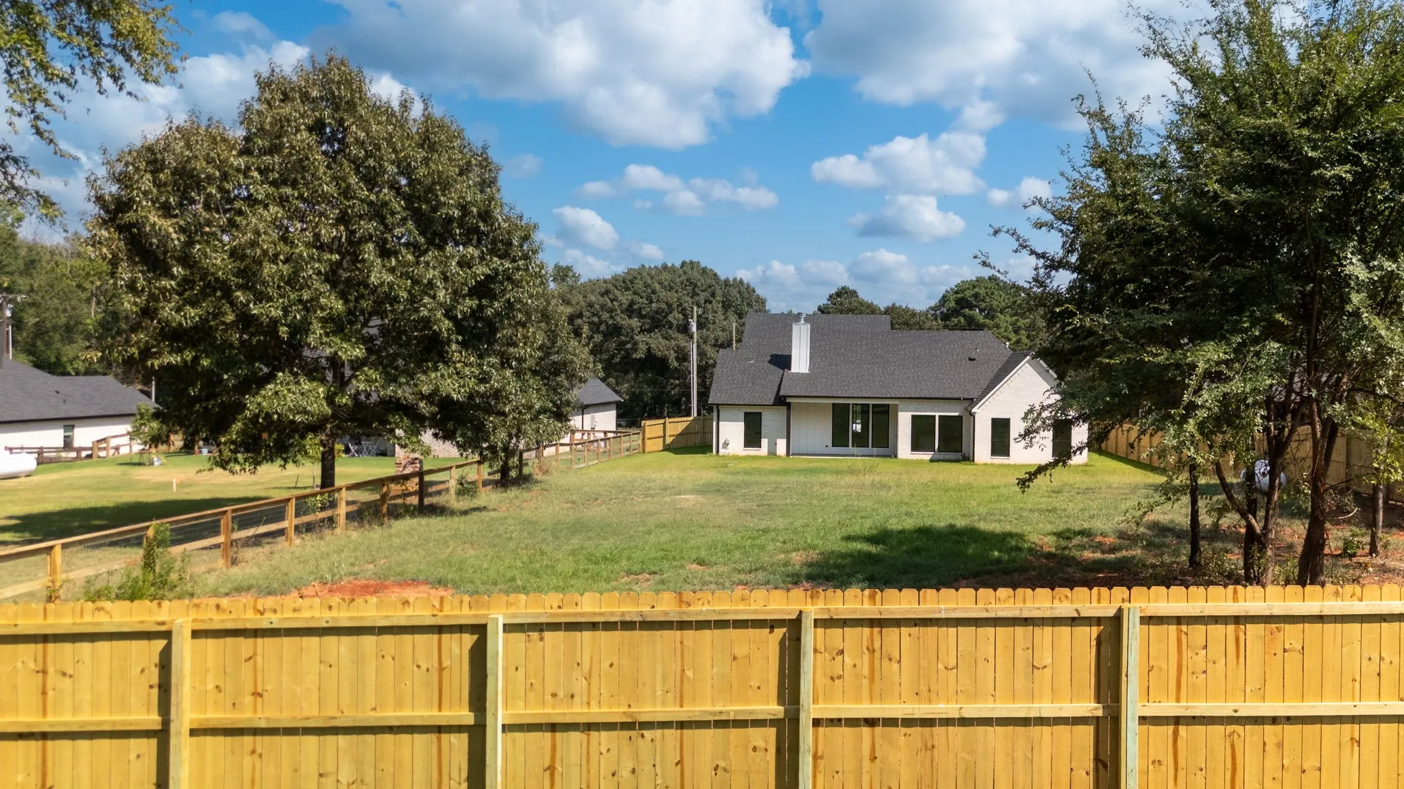 Expansive backyard featuring a new privacy fence, partial split-rail fencing, a manicured lawn, and mature trees