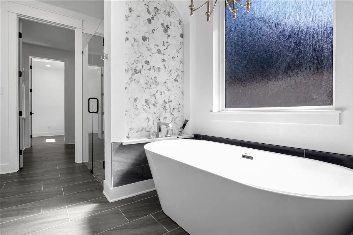 Freestanding soaking tub with a wall-mounted faucet, complemented by a tiled accent wall and large format tile flooring