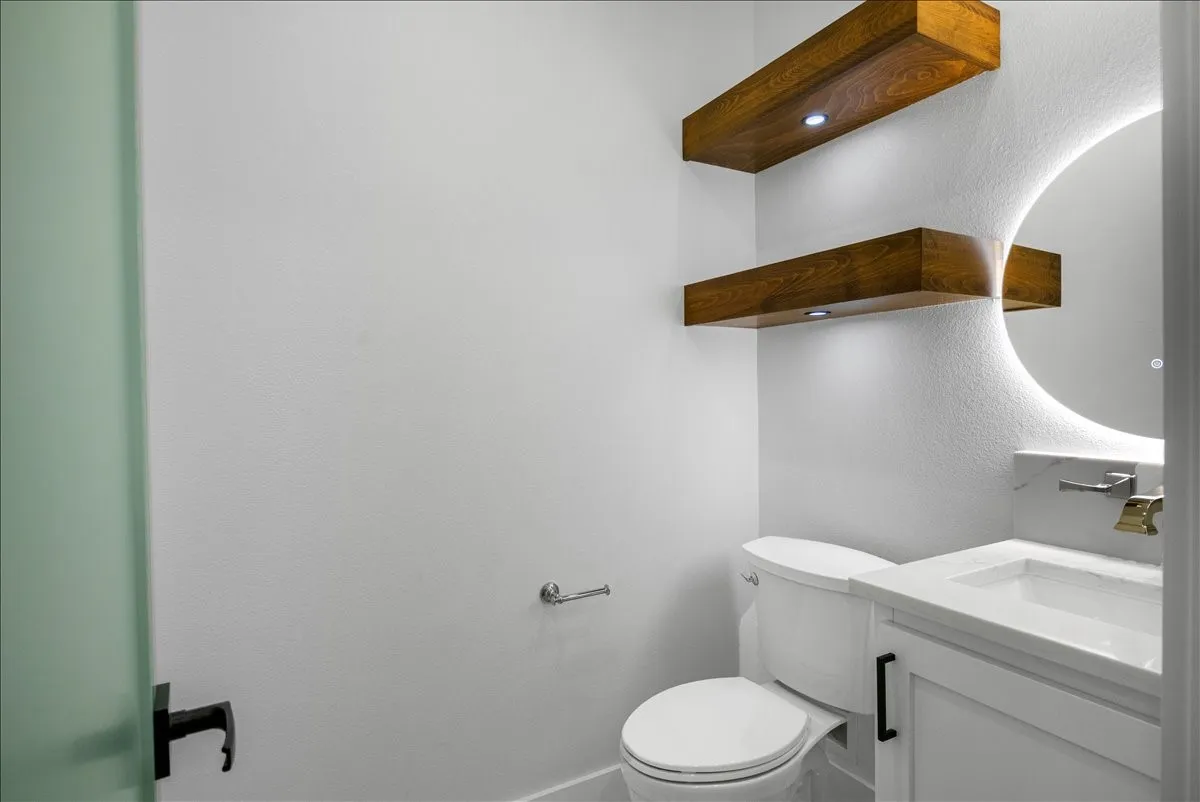 White vanity with a rectangular undermount sink, a stone countertop, and a circular back-lit mirror