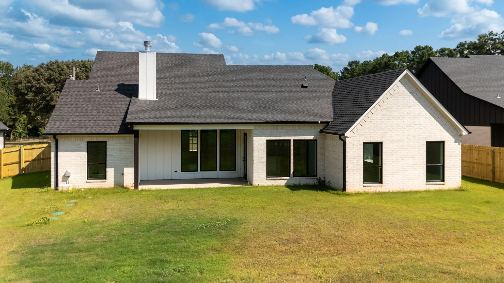 Expansive backyard featuring a manicured lawn, partial wood fencing, a covered patio area, and a white brick exterior