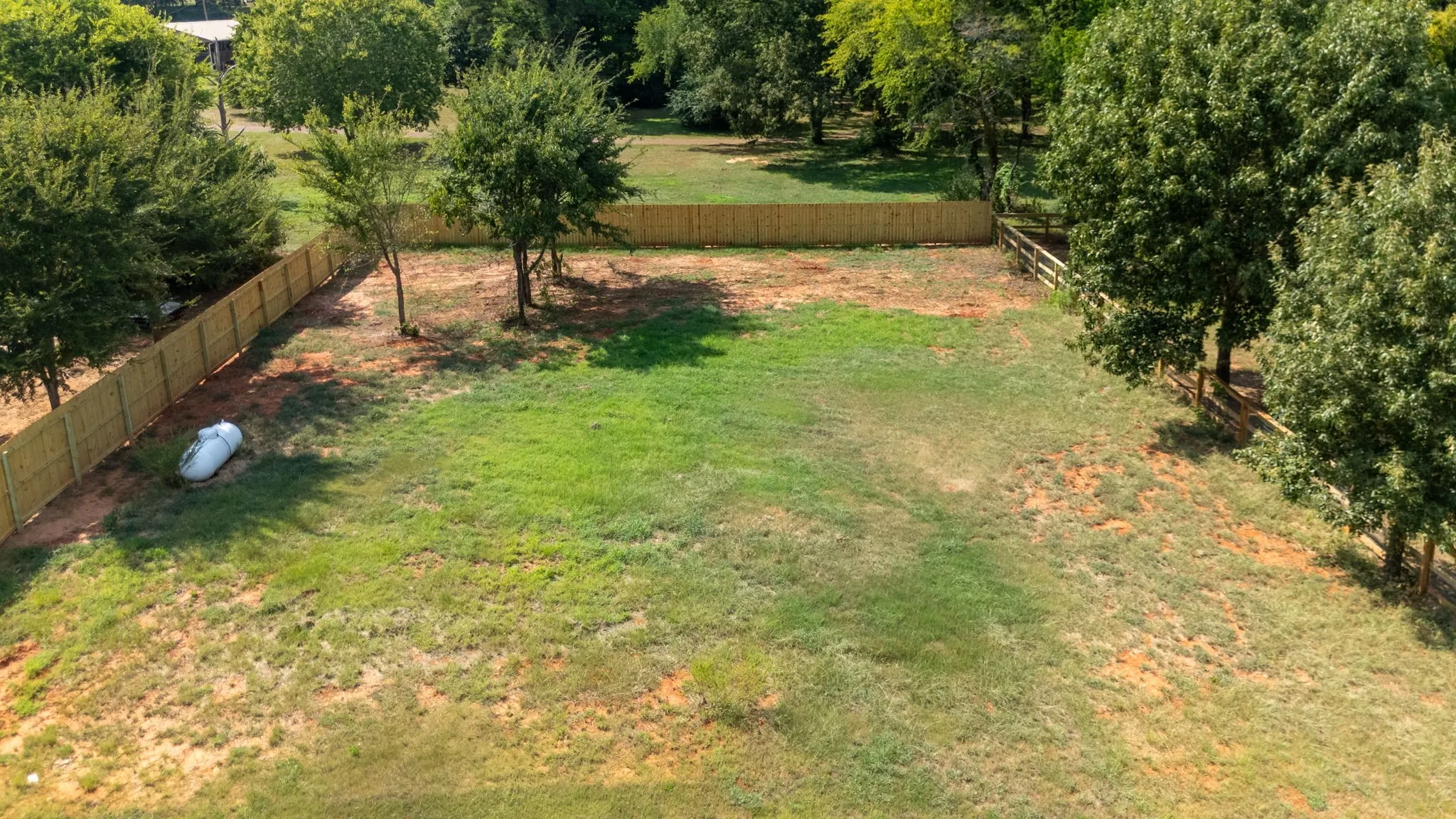 Expansive property featuring mature trees, partial privacy fencing, and a large grassy area