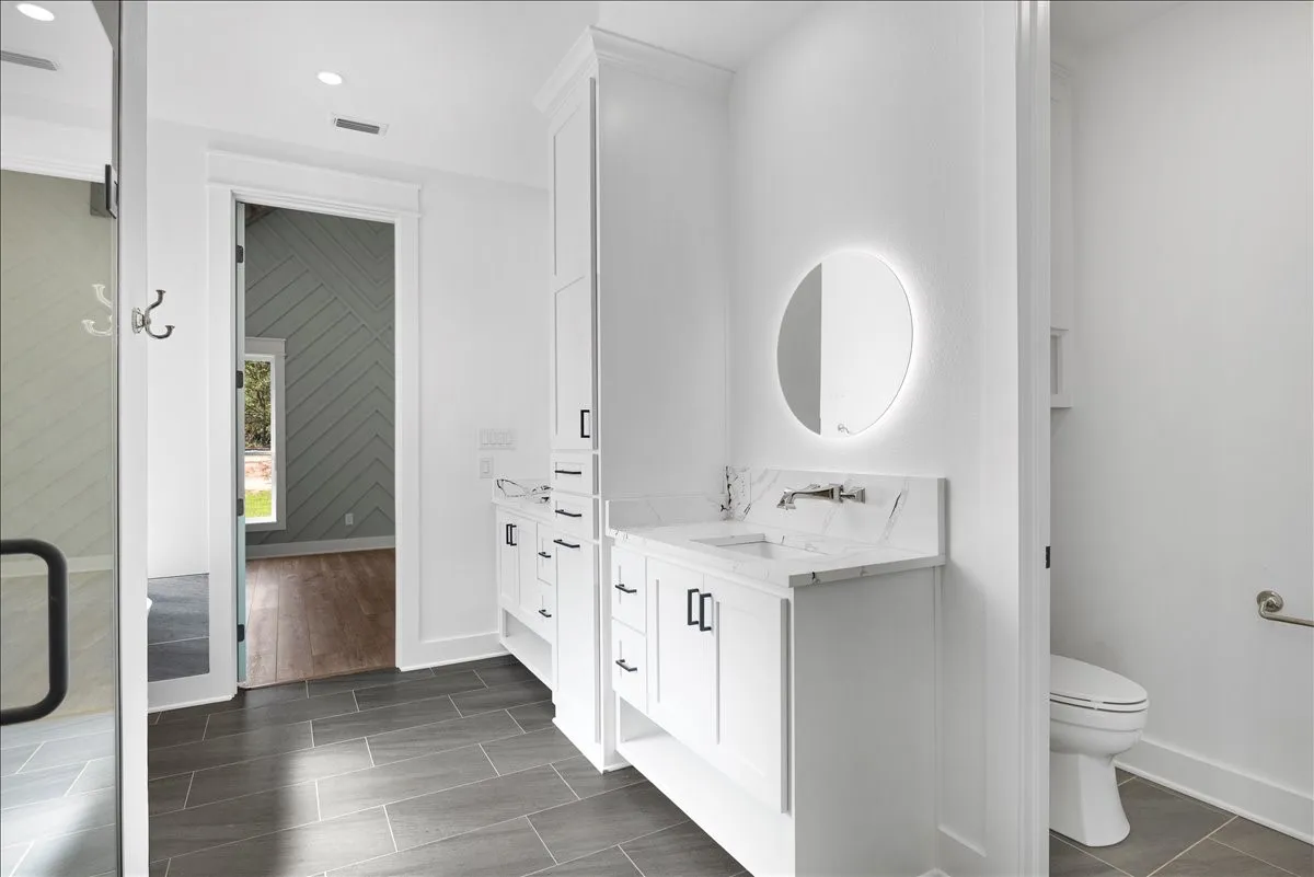 White double vanity with integrated sinks, back-lit round mirrors, and wall-mounted faucets