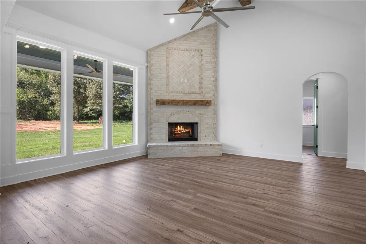 Vaulted ceiling with a ceiling fan, corner fireplace with a stone surround and wood mantel, wood-finish flooring, and multiple large windows