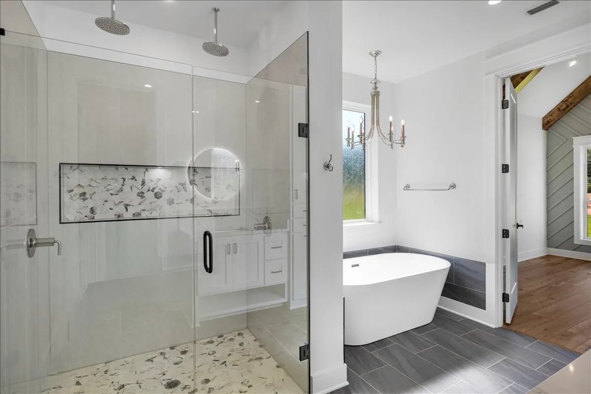 Walk-in shower with dual rain shower heads, freestanding soaking tub, wood-finish flooring, and a chandelier light fixture