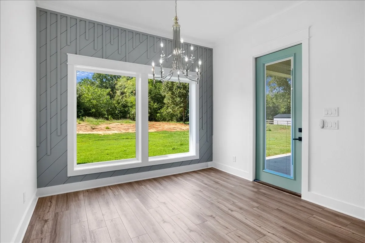 Wood-finish flooring, accent wall with geometric paneling, contemporary chandelier, double window, and a full-light glass door with a teal frame