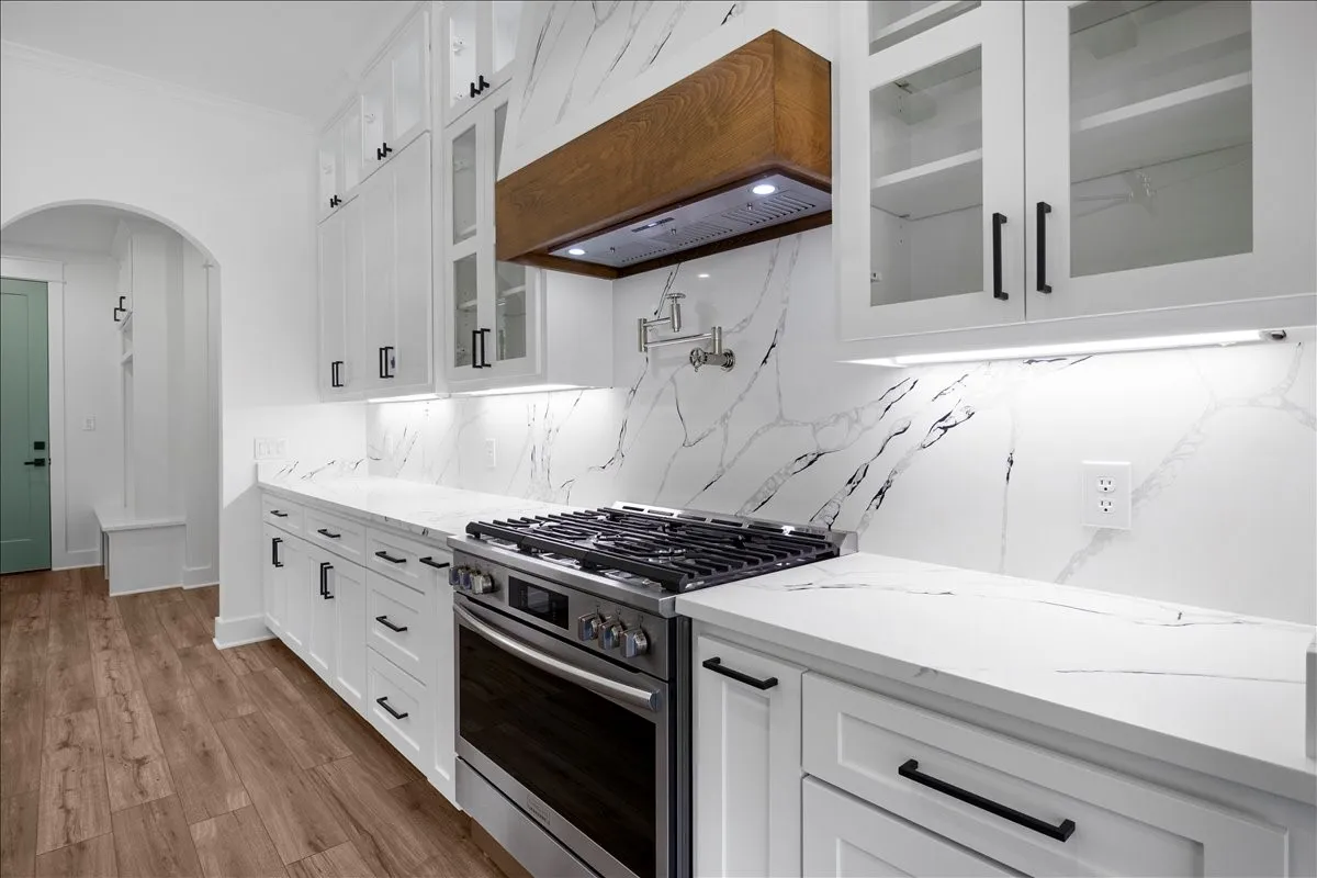 White cabinetry with matte black hardware, integrated stainless steel range, white countertops, full-height backsplash, and wood-finish flooring