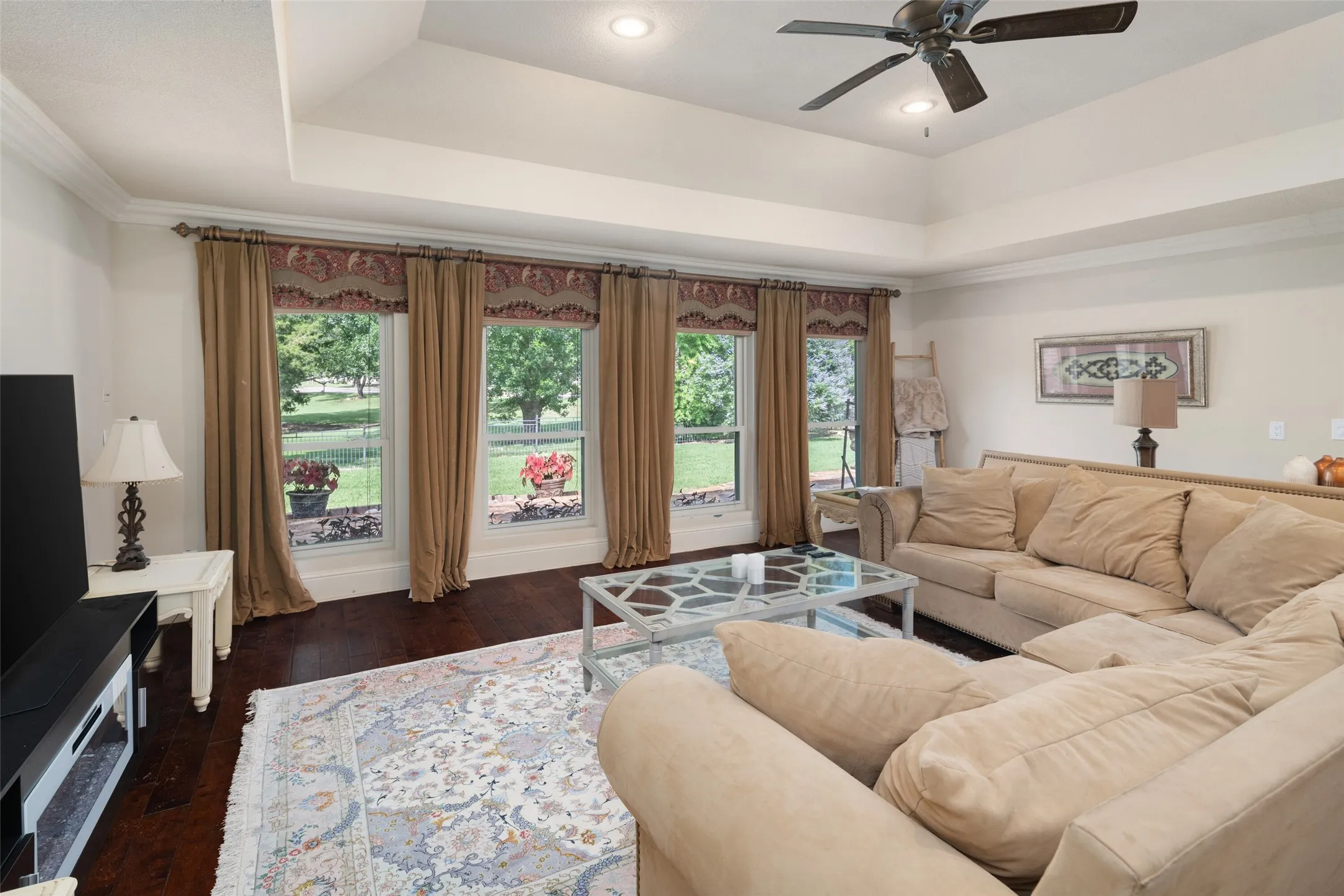 Living room featuring a raised ceiling, a ceiling fan, dark wood finished floors, and recessed lighting