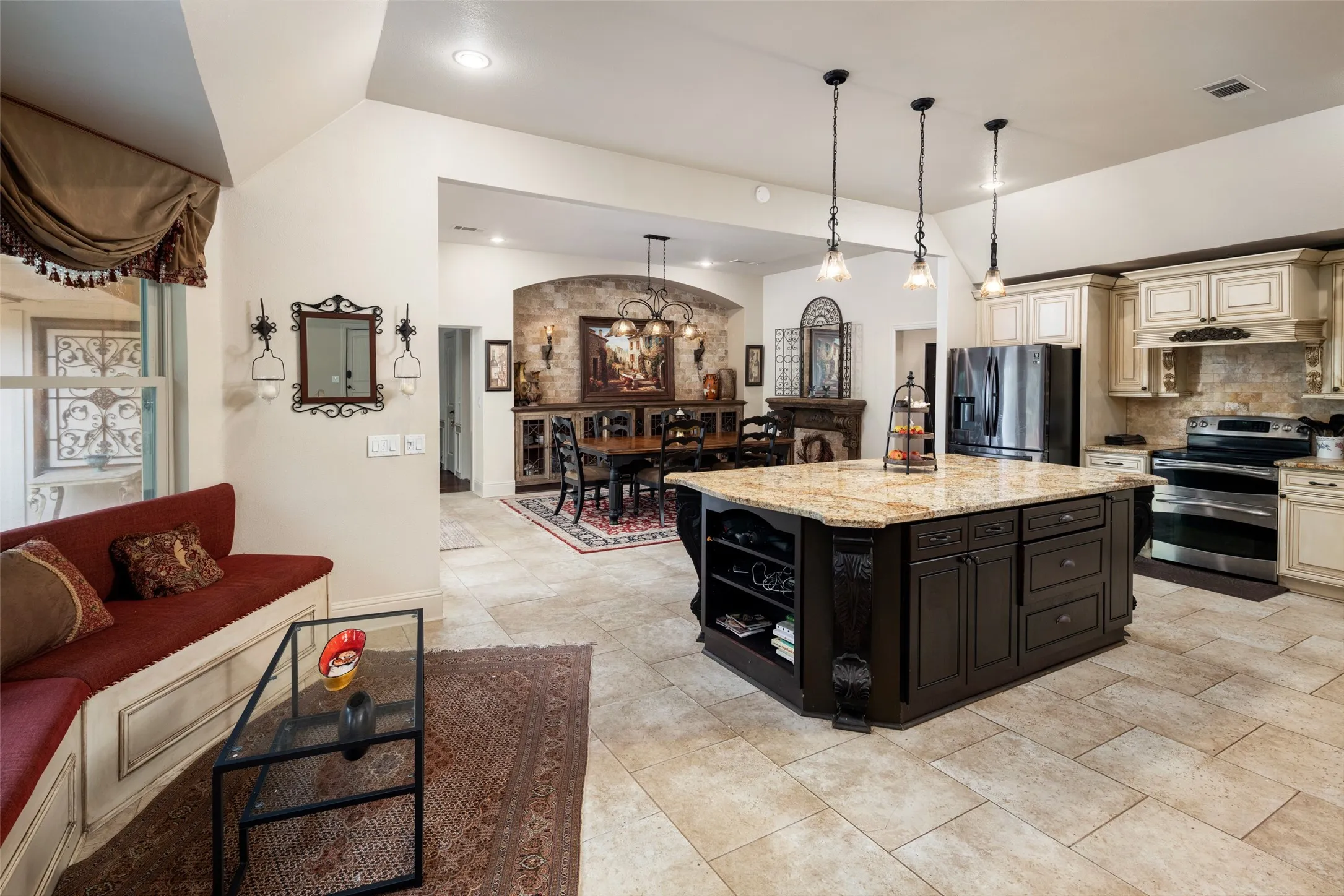 Kitchen with stainless steel appliances, cream cabinetry, dark cabinets, light stone countertops, and tasteful backsplash