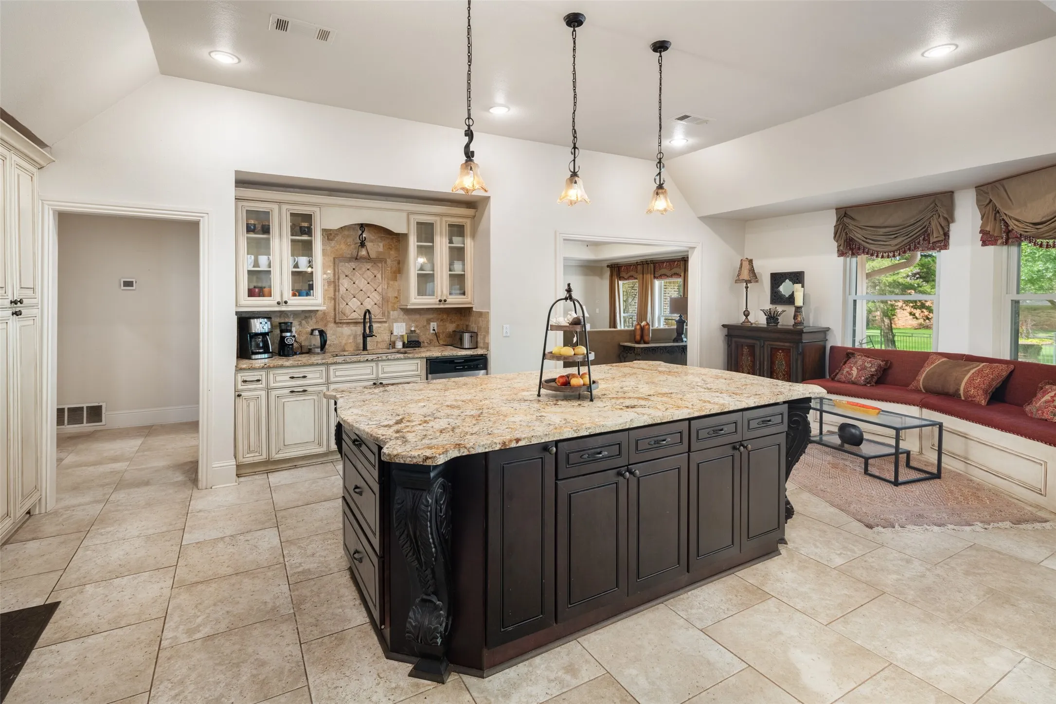 Kitchen featuring lofted ceiling, dark cabinetry, tasteful backsplash, pendant lighting, and light stone counters