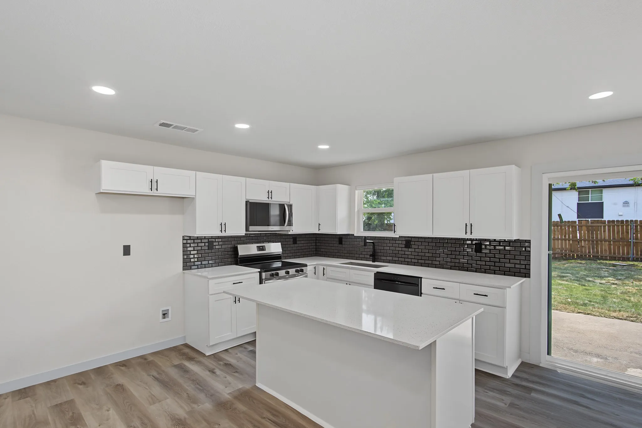 Contemporary kitchen featuring white cabinetry, a central island with a solid surface countertop, stainless steel appliances, a dark subway tile backsplash, and wood-finish flooring