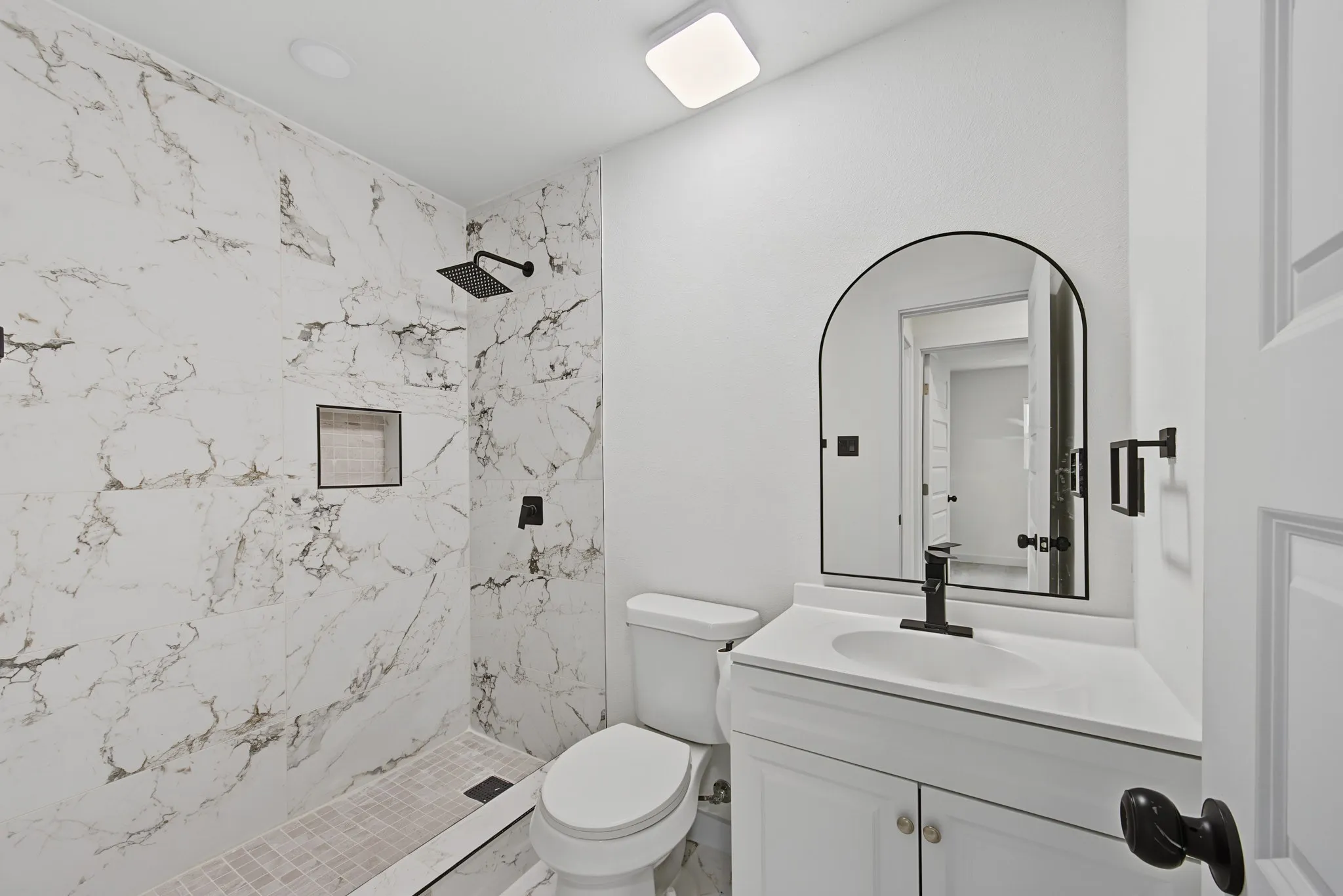 Modern bathroom featuring a walk-in shower with large format marble-look tile, a recessed shower niche, and matte black fixtures