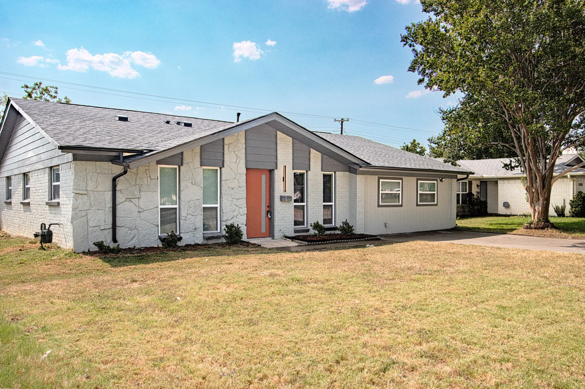 Exterior featuring a stone facade, a gray shingled roof, an orange front door, and a paved driveway