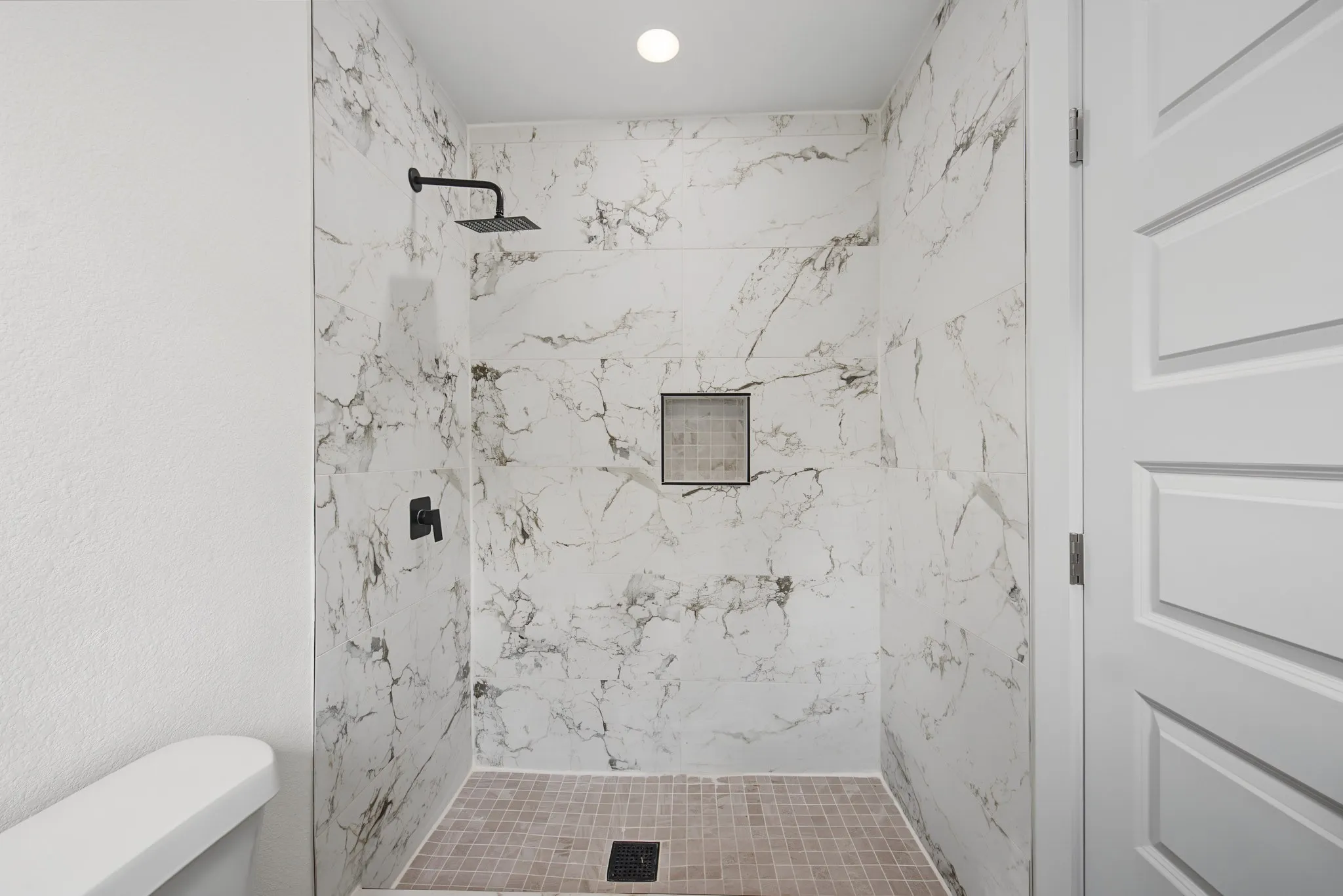 Walk-in shower featuring large format veined wall tiles, a recessed niche, a square rainfall shower head, and matte black fixtures