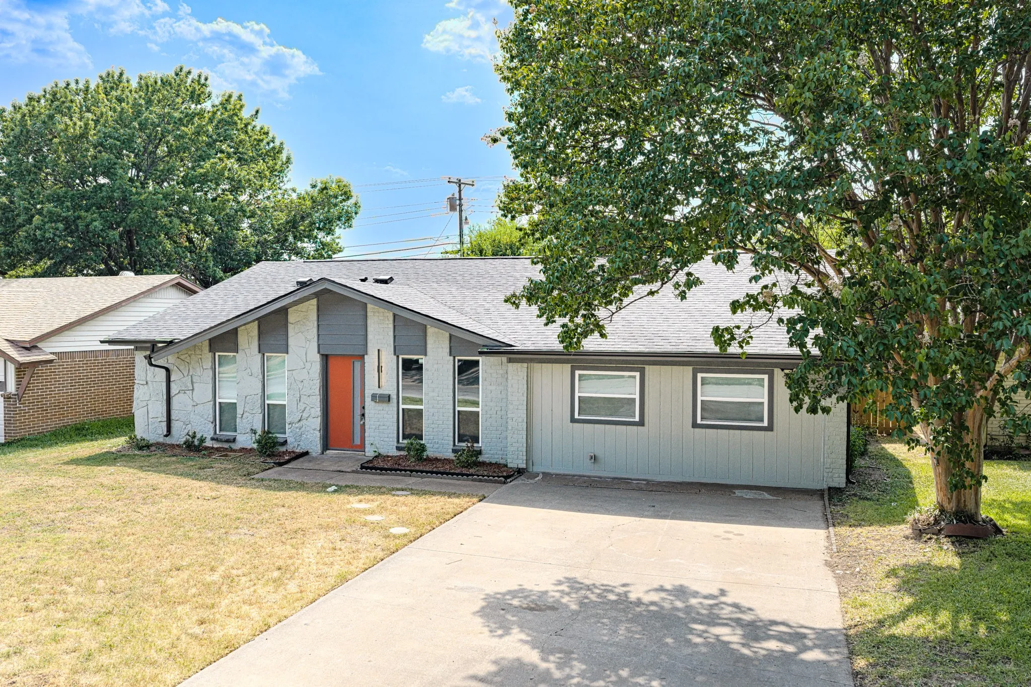 Exterior featuring stone facade, grey siding, a bright orange front door, and a concrete driveway
