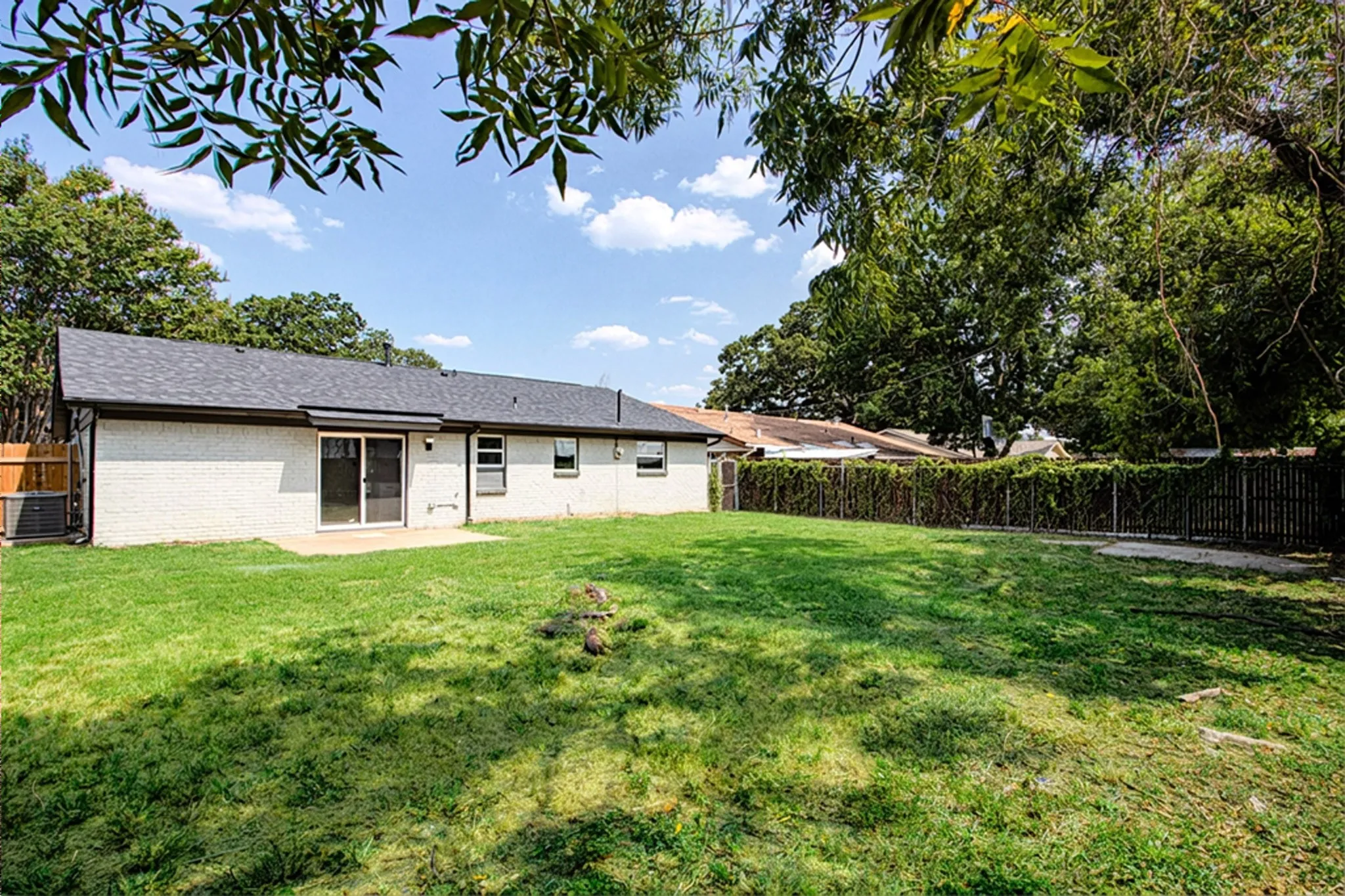 Expansive rear yard featuring a grass lawn, mature perimeter trees, and a privacy fence