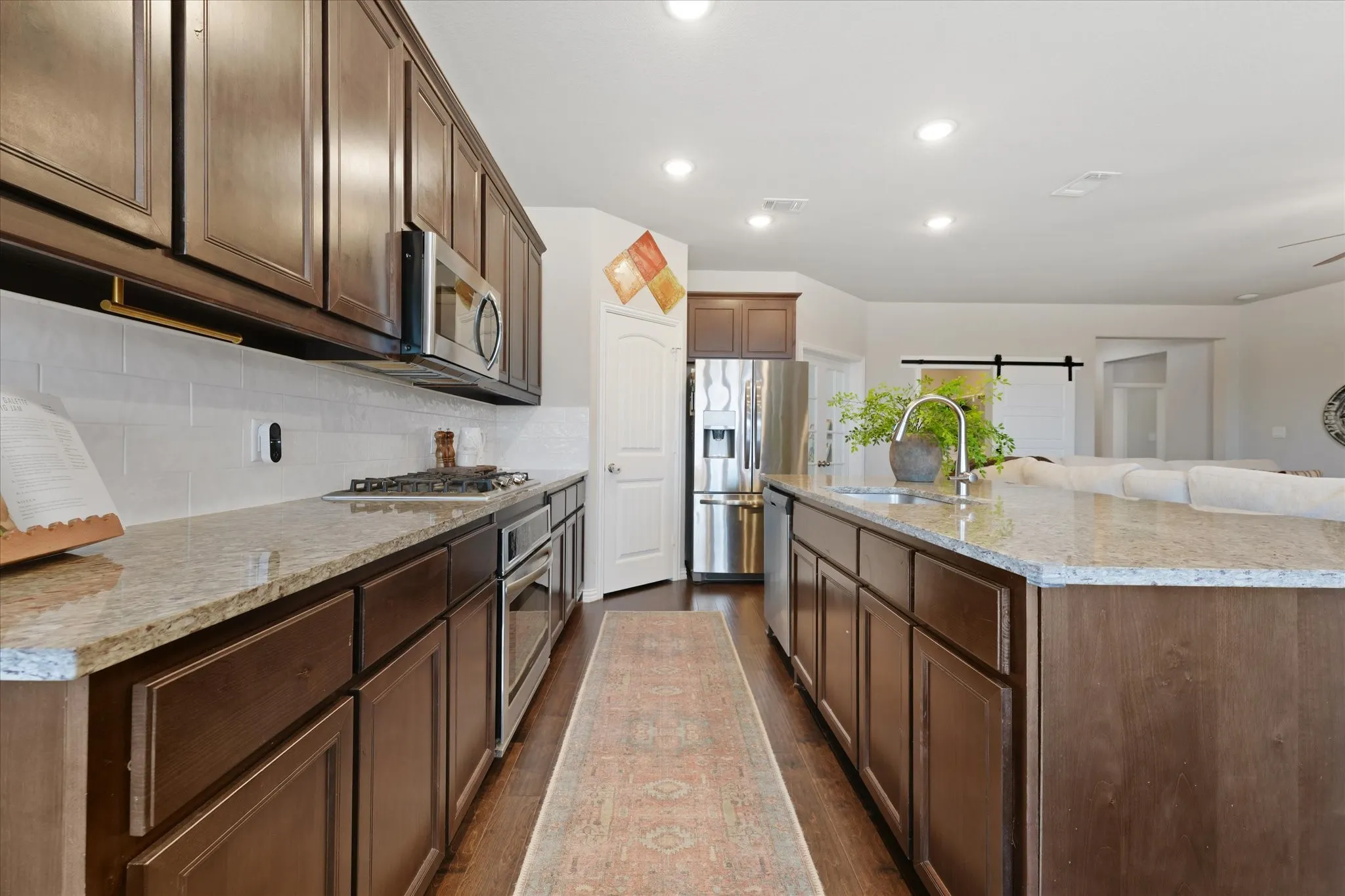 Kitchen featuring rich wood cabinetry, granite countertops, a built-in stainless steel gas range, oven, and microwave, and a white subway tile backsplash