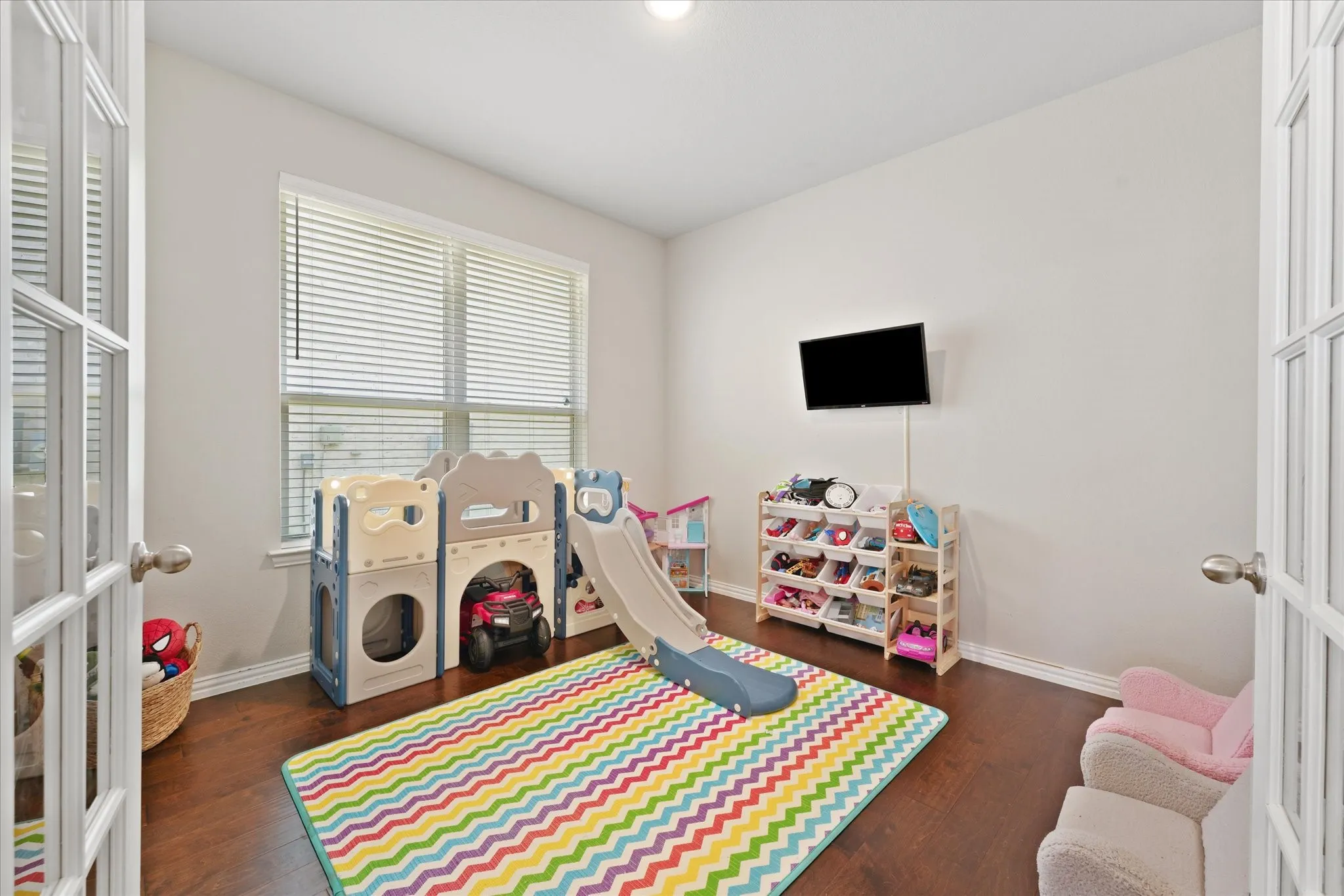 Interior room featuring wood-finish flooring, white walls, and a mounted television