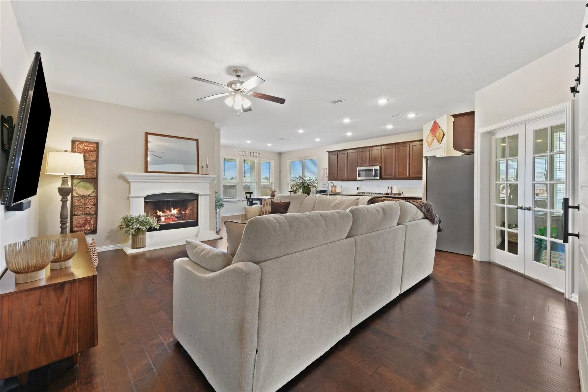 Spacious living area featuring dark wood-finish flooring, a white mantel fireplace, and a ceiling fan