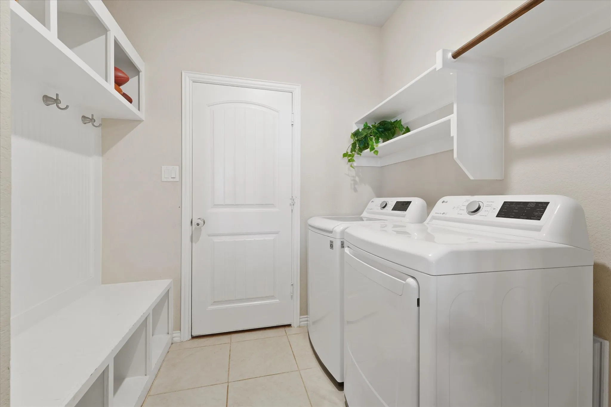 Laundry area with light tile flooring, built-in mudroom bench with storage cubbies, and overhead shelving with integrated hanging rod