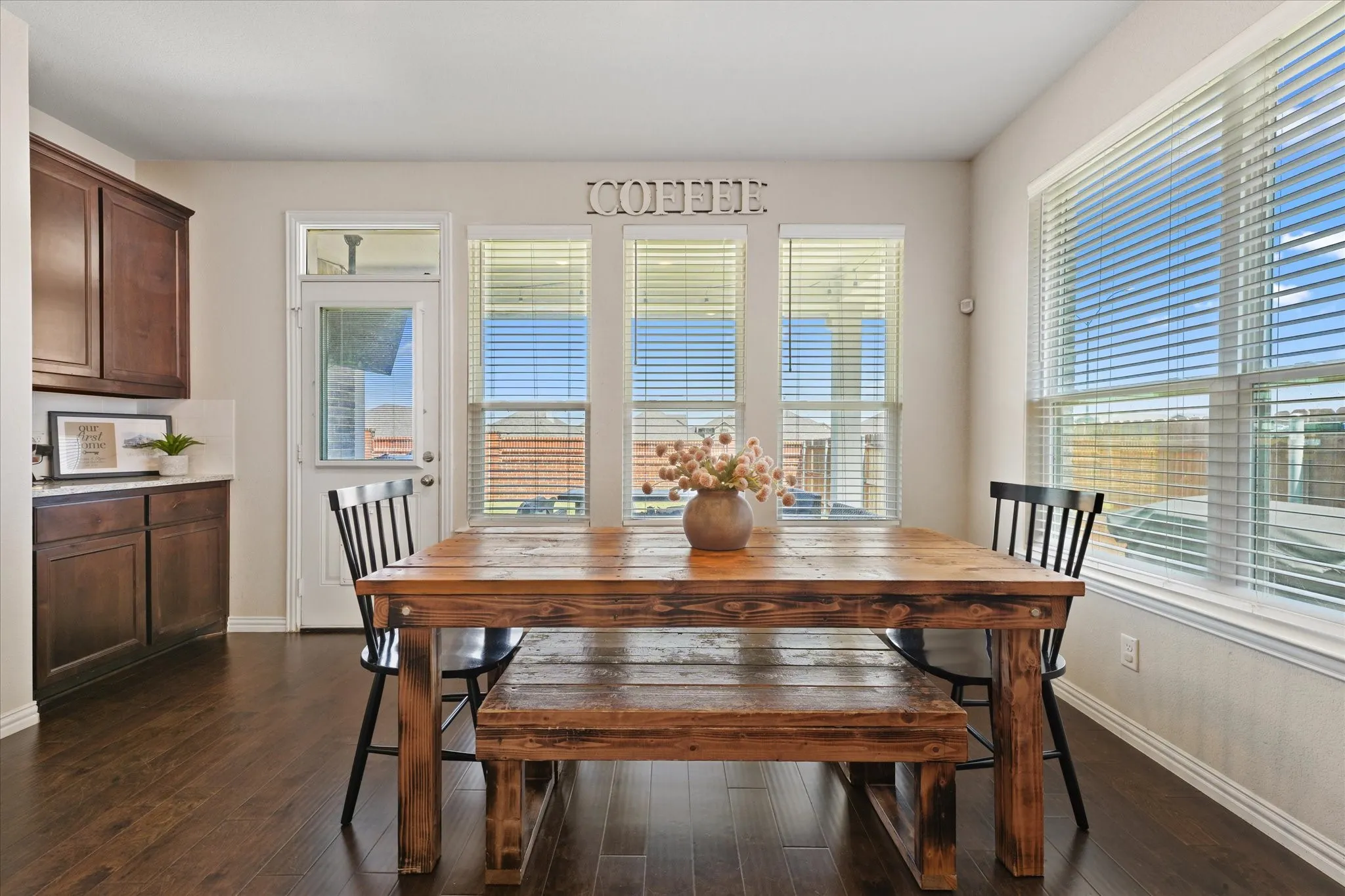 Dining area featuring rich wood-finish flooring, multiple large windows with horizontal blinds, a glass-paneled exterior door, and built-in cabinetry with a light-toned countertop