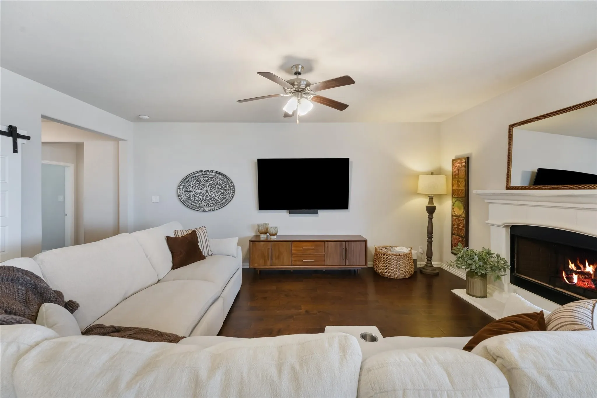 Living area featuring wood-finish flooring, a ceiling fan with light fixture, and a fireplace with a white mantel and hearth