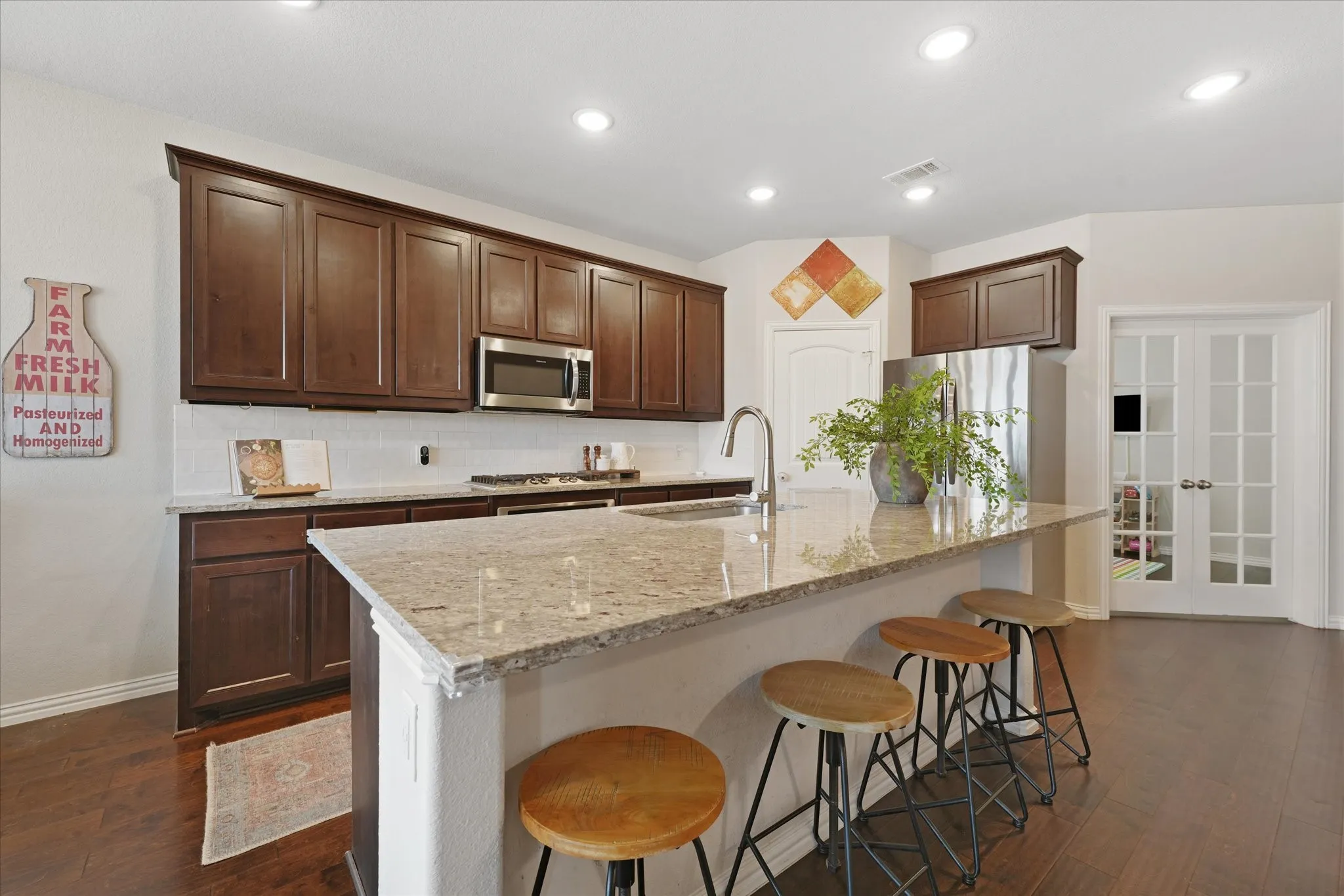 Kitchen featuring an expansive island with a granite countertop, dark wood-finish cabinetry, stainless steel appliances, and wood-finish flooring