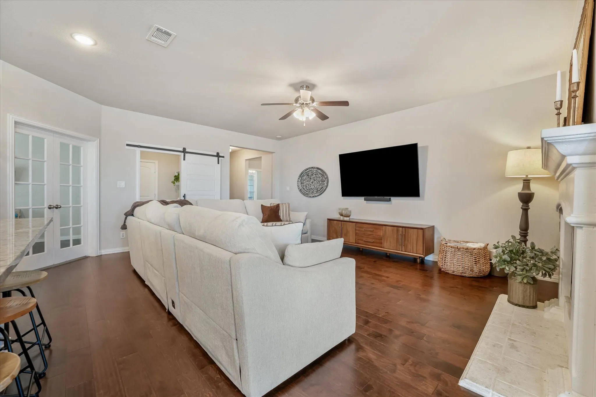 Living area featuring rich wood-finish flooring, a white mantel fireplace, ceiling fan with integrated lighting, and recessed ceiling lights