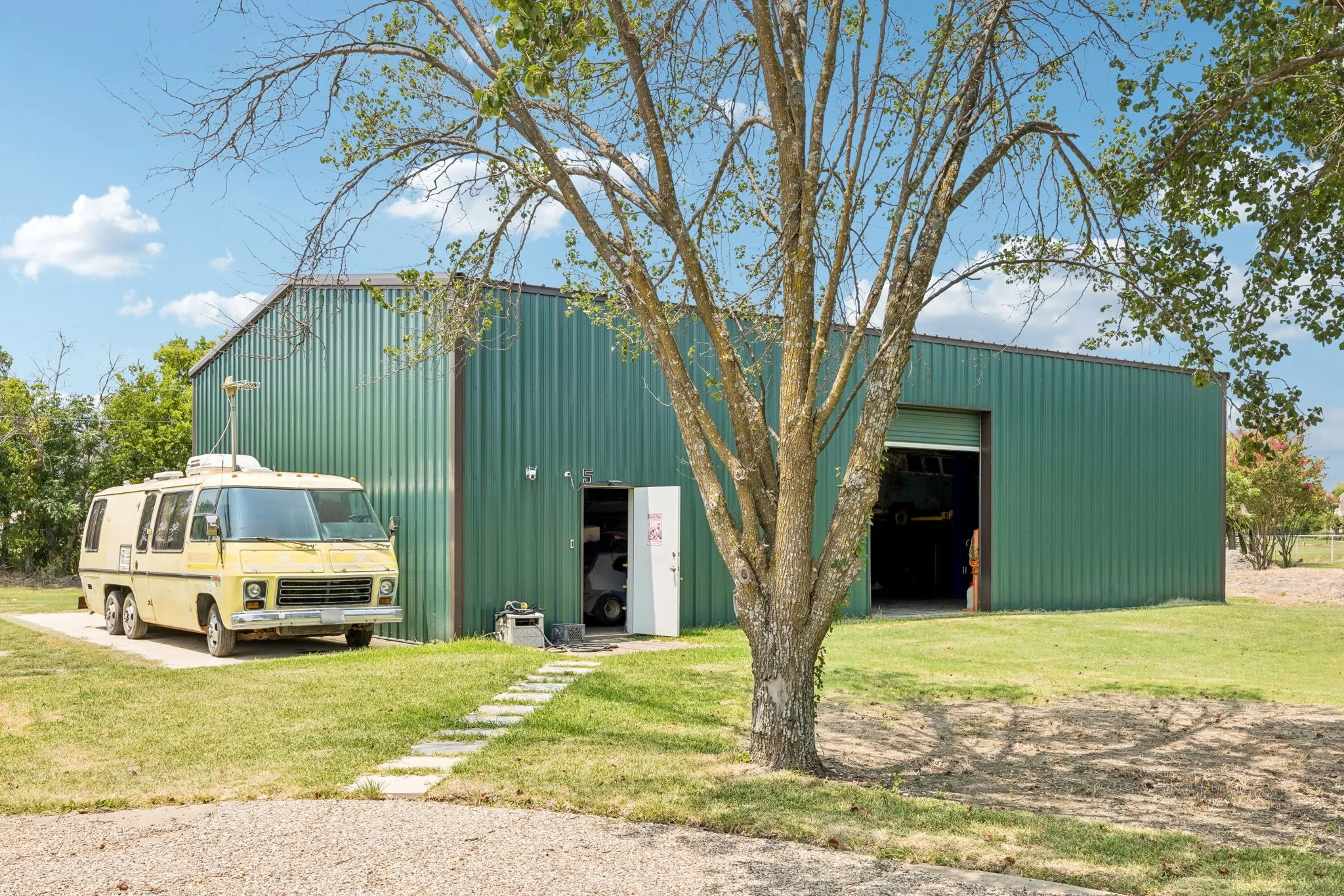 Green corrugated metal building with a large open bay door and a smaller personnel door