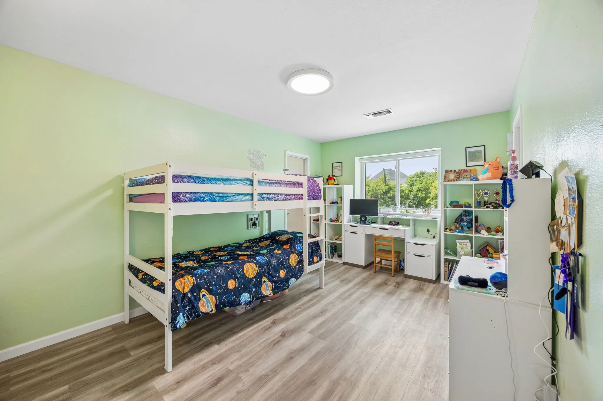 Interior room featuring light green walls, wood-finish flooring, a flush-mount ceiling light, and a window with exterior views
