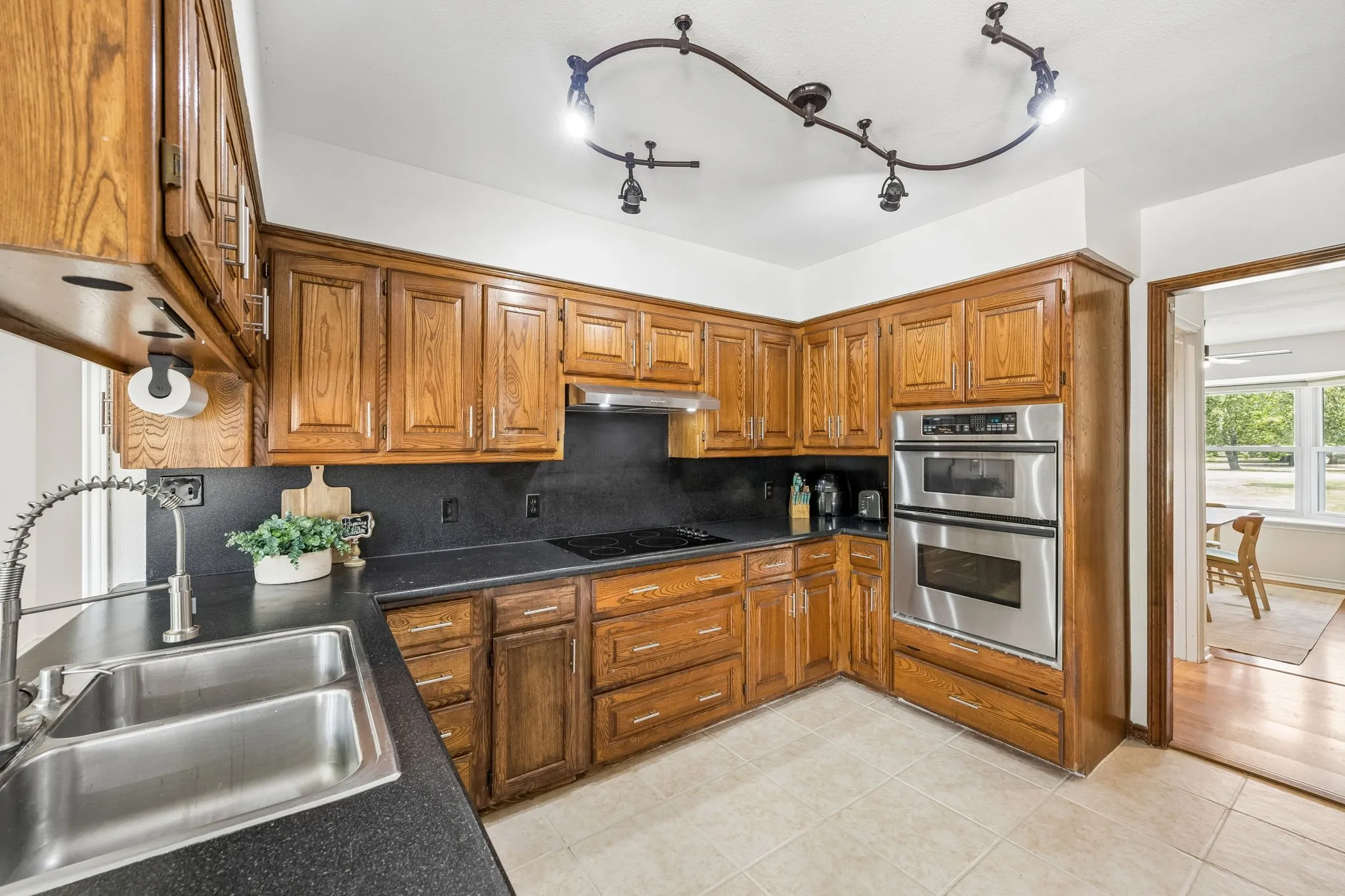 Kitchen featuring wood cabinetry, dark countertops, a double basin stainless steel sink with a high-arc faucet, and integrated stainless steel double ovens