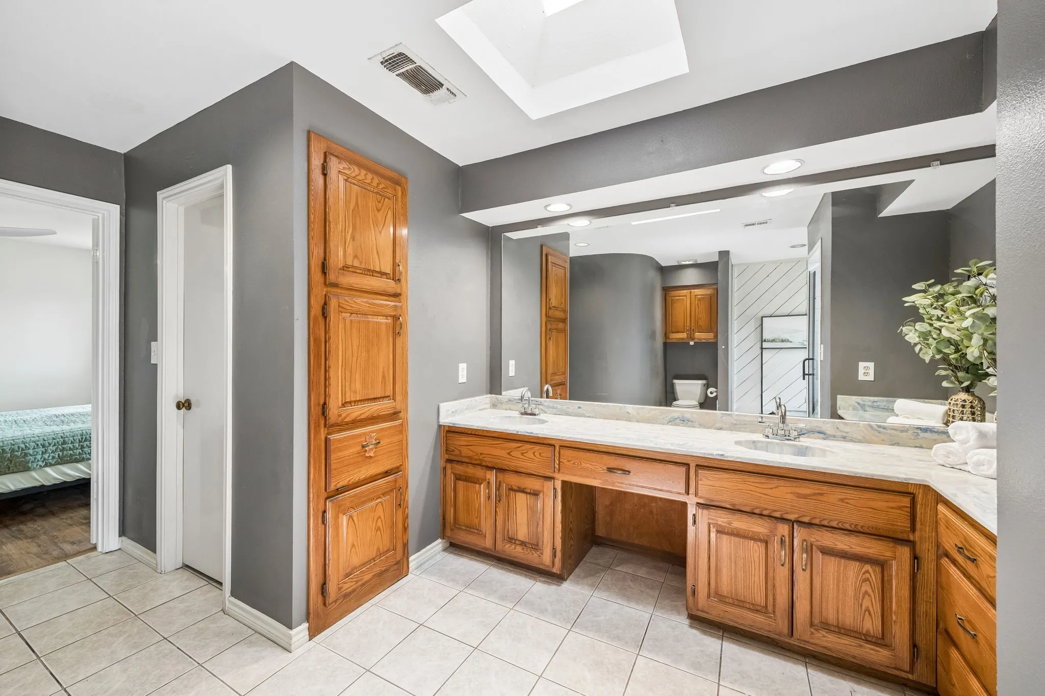 Bathroom featuring a dual vanity with a light-toned countertop, wood cabinetry, and a large mirror