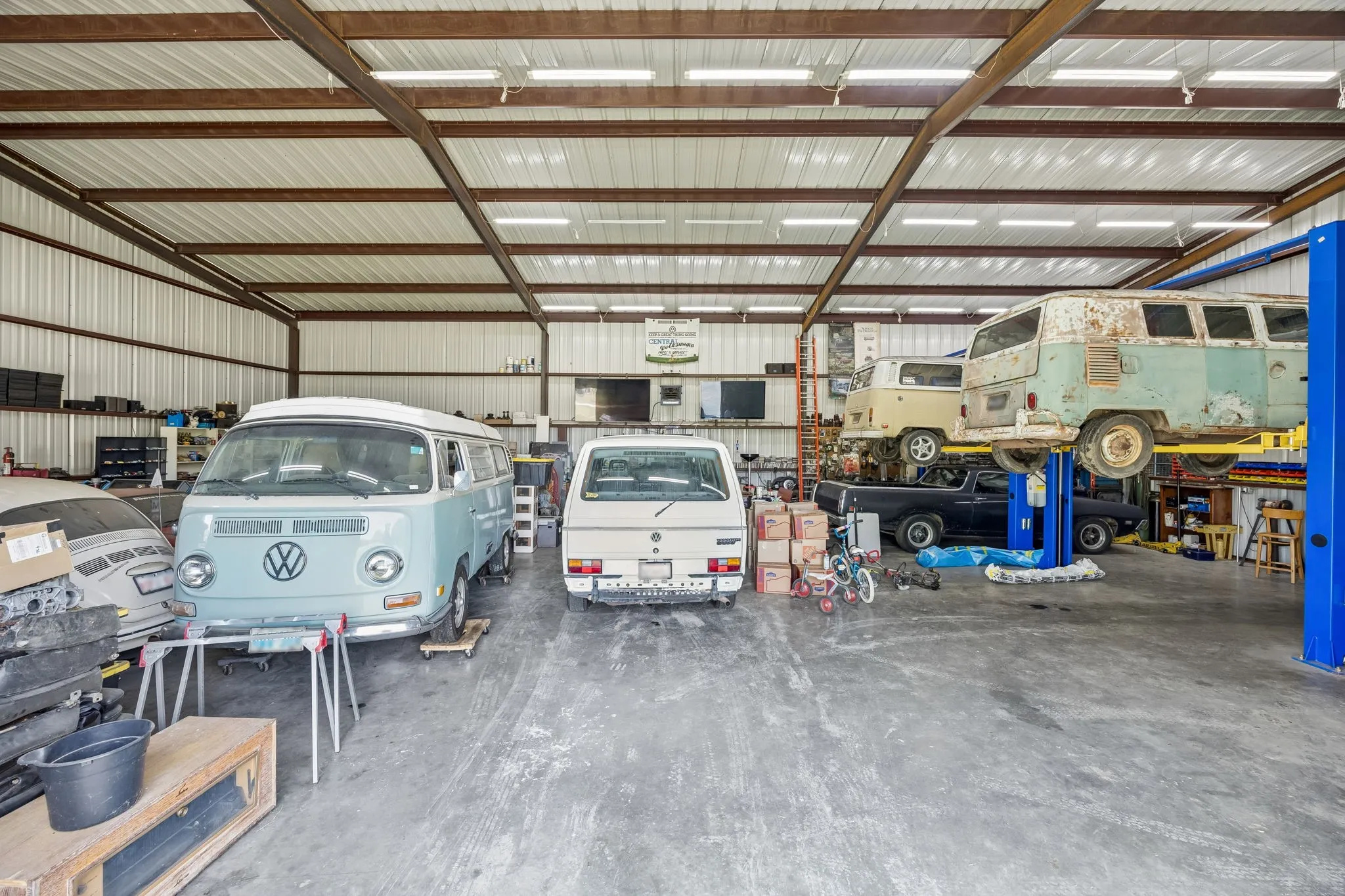 Spacious commercial building featuring a corrugated metal exterior, exposed steel beam construction, overhead fluorescent lighting, and a concrete floor