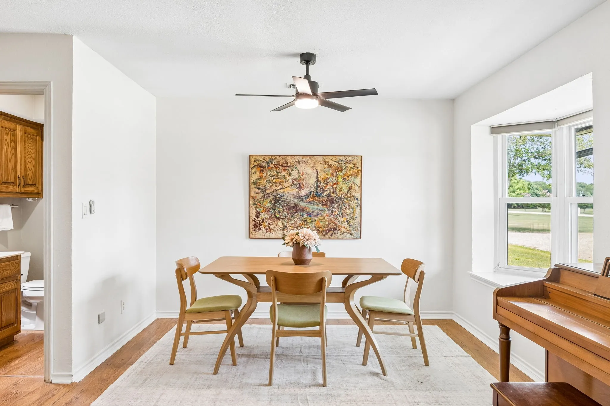 Dining area featuring light wood-finish flooring, a contemporary ceiling fan with integrated lighting, and a bay window